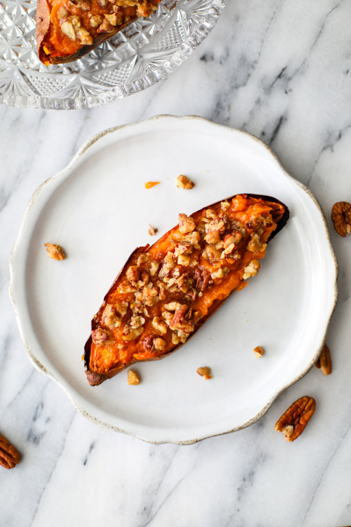 A potato topped with pecans and brown sugar clusters on a rustic white plate.
