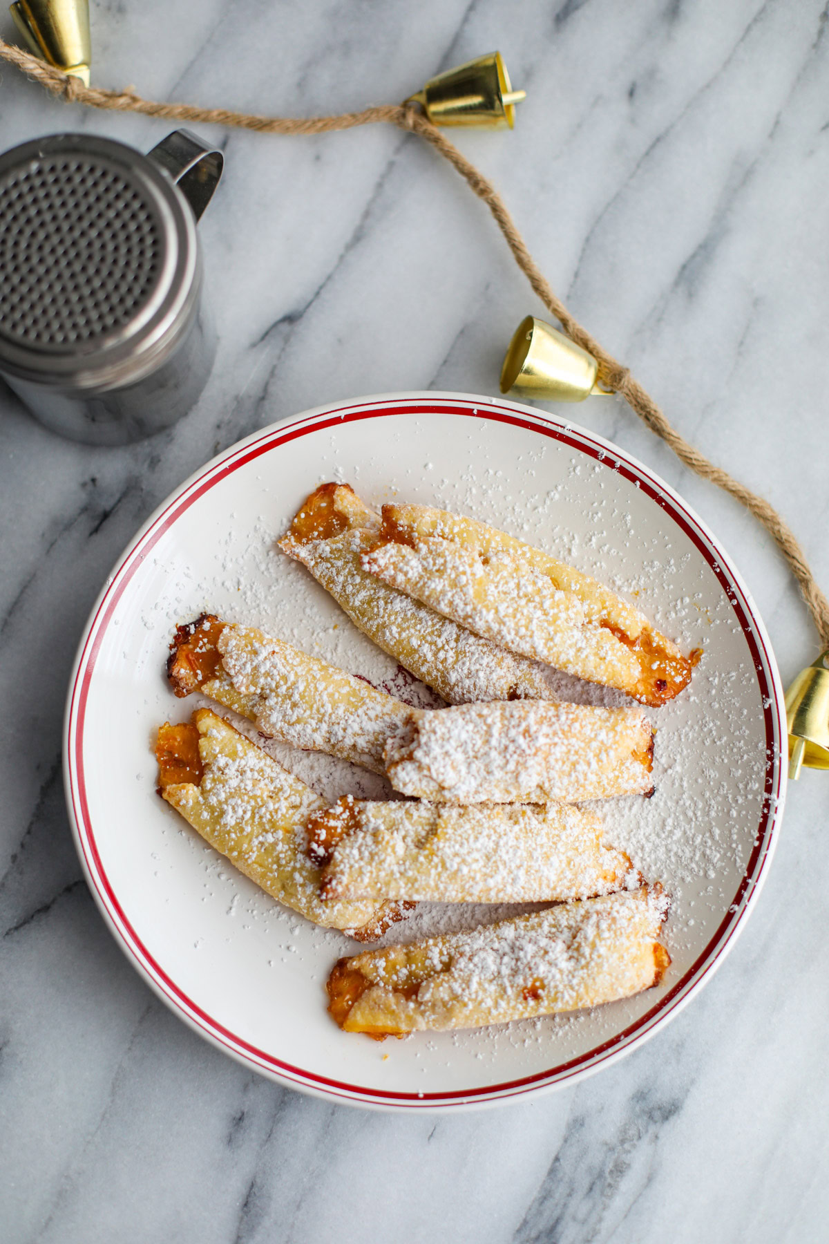 A white Christmas plate with apricot cream cheese cookies and a silver powdered sugar shaker.