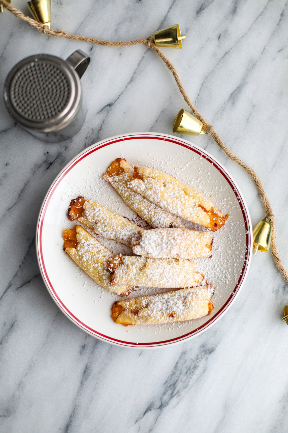 A white Christmas plate with apricot cream cheese cookies and a silver powdered sugar shaker.