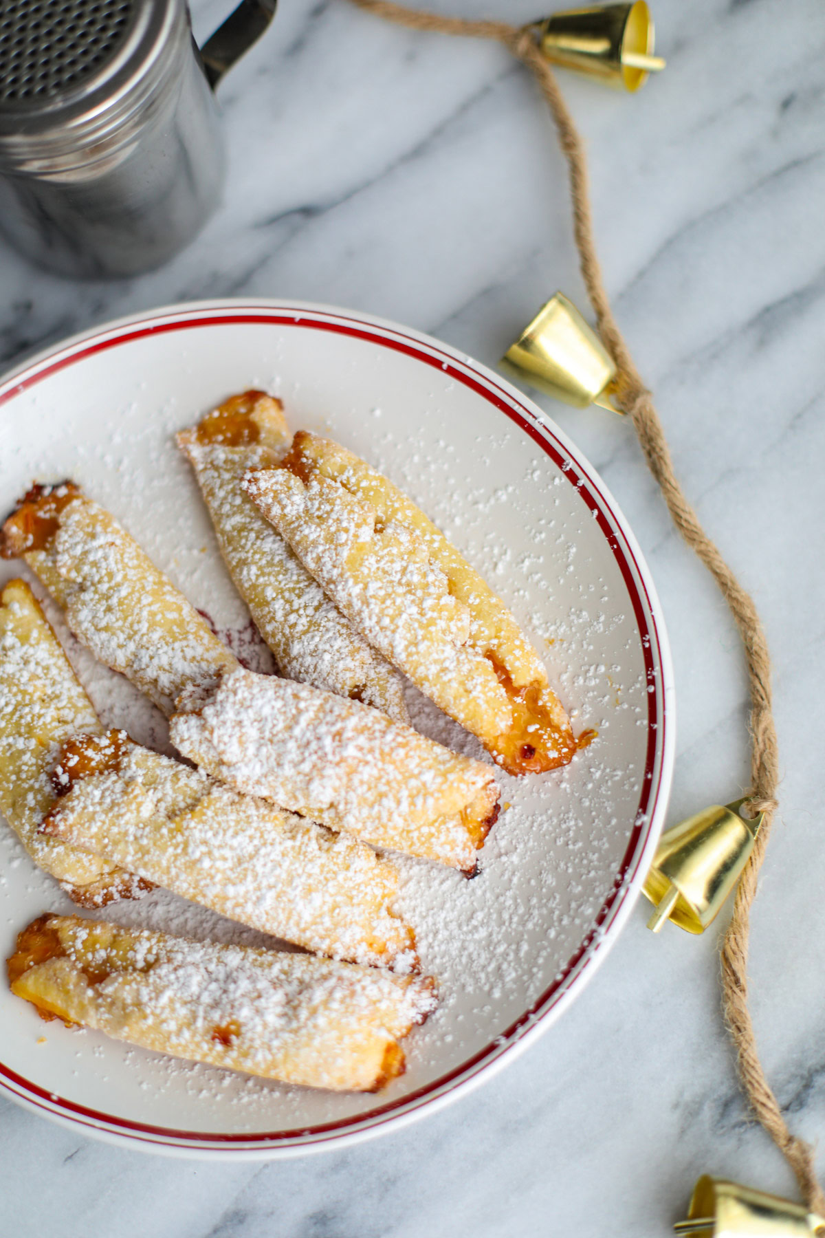 A close up of a white Christmas plate with apricot cream cheese cookies and a silver powdered sugar shaker.
