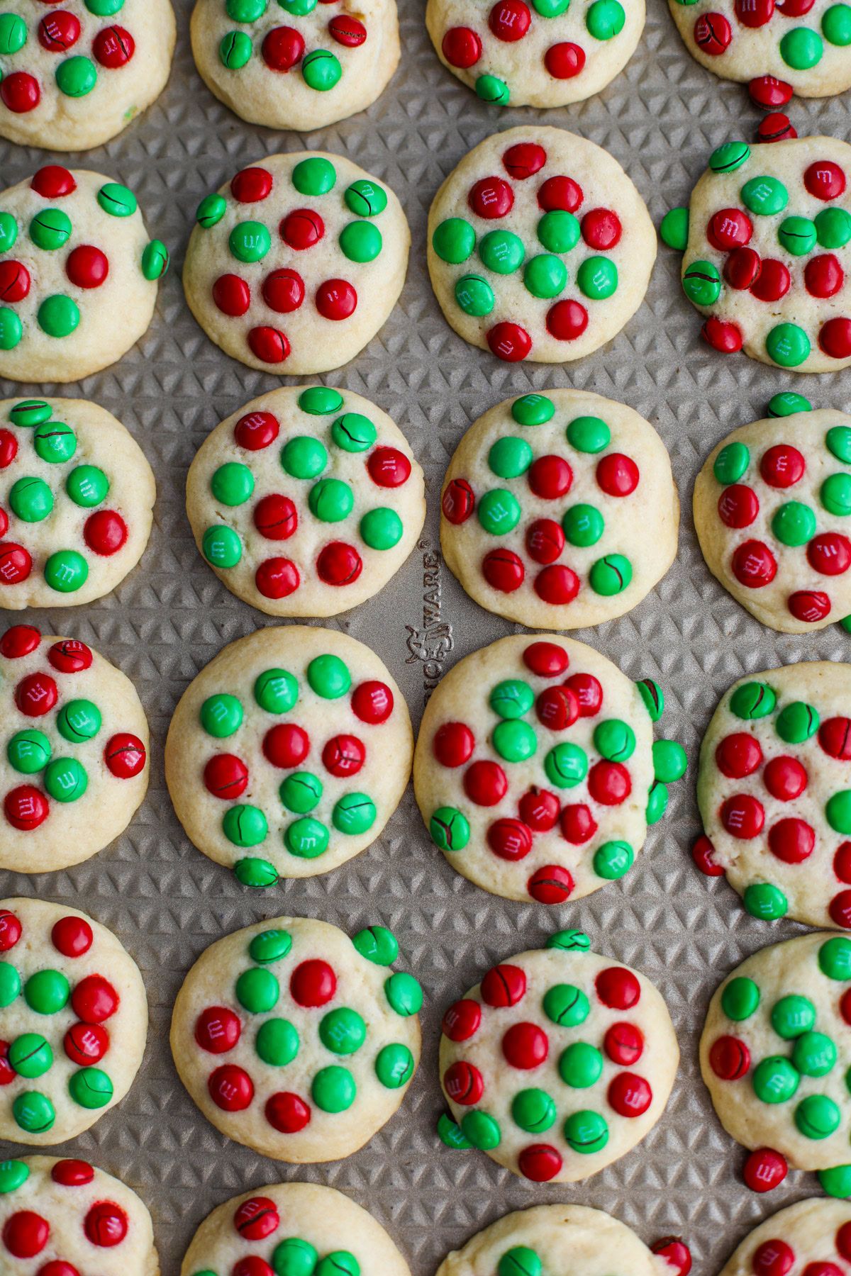 An up close of a gold sheet tray filled with rows of red and green M&M butter cookies.