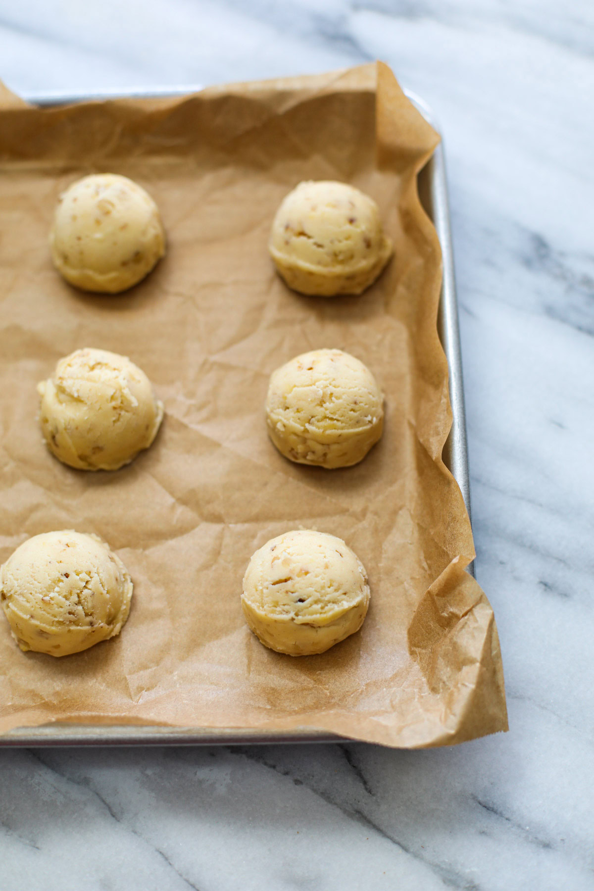 Scoops of cookie dough on a parchment lined baking sheet. 