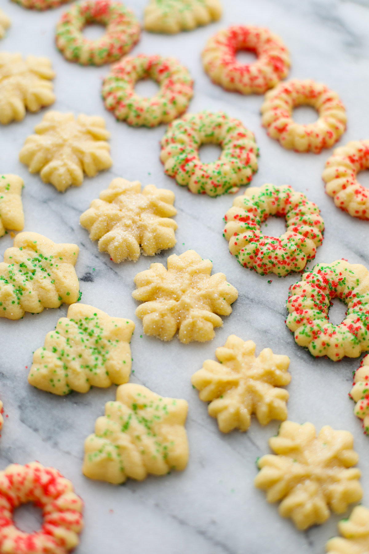 Rows of red and green sprinkled Christmas spritz cookies shaped into wreaths, trees, and snowflakes.