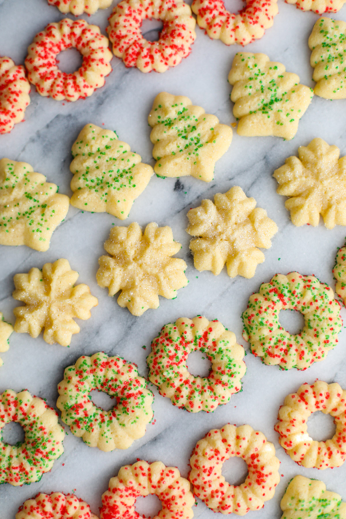Rows of red and green sprinkled butter cookies shaped into wreaths, trees, and snowflakes.