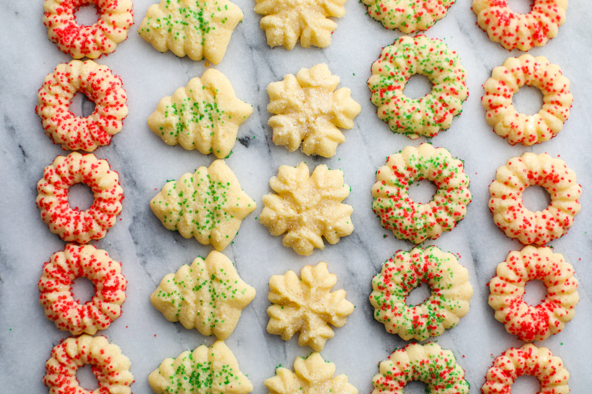 Rows of red and green sprinkled Christmas spritz cookies shaped into wreaths, trees, and snowflakes.