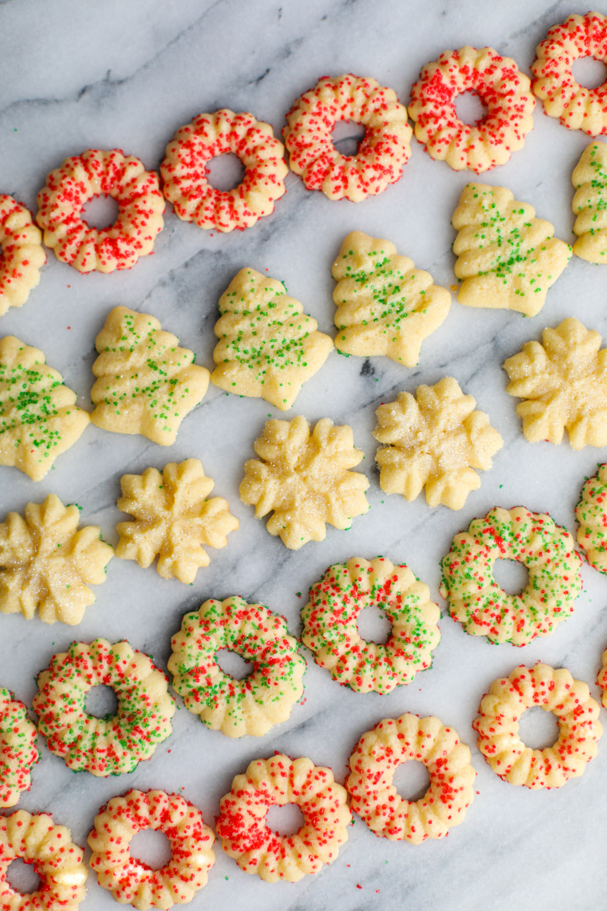 Rows of red and green sprinkled butter cookies shaped into wreaths, trees, and snowflakes.