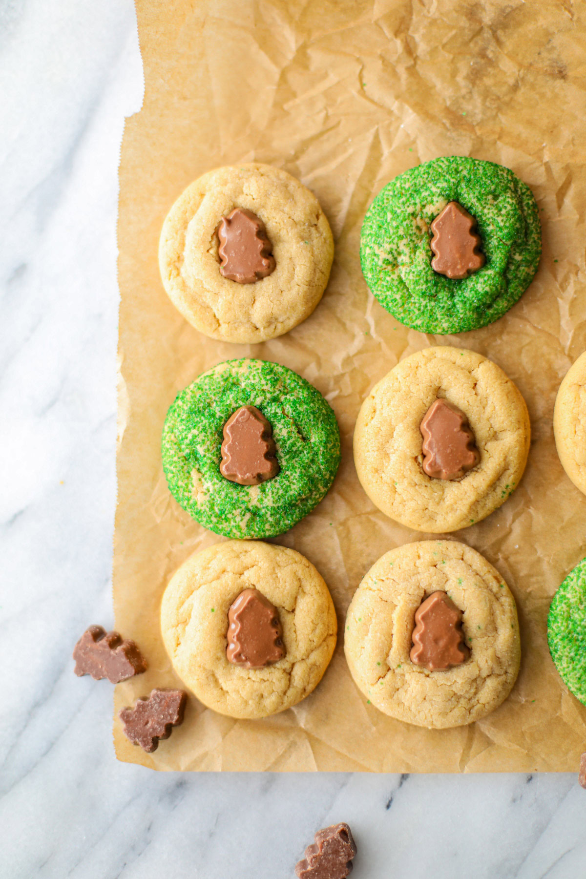 Brown parchment paper with Peanut Butter Blossoms lined up in rows with several loose Christmas tree chocolates.