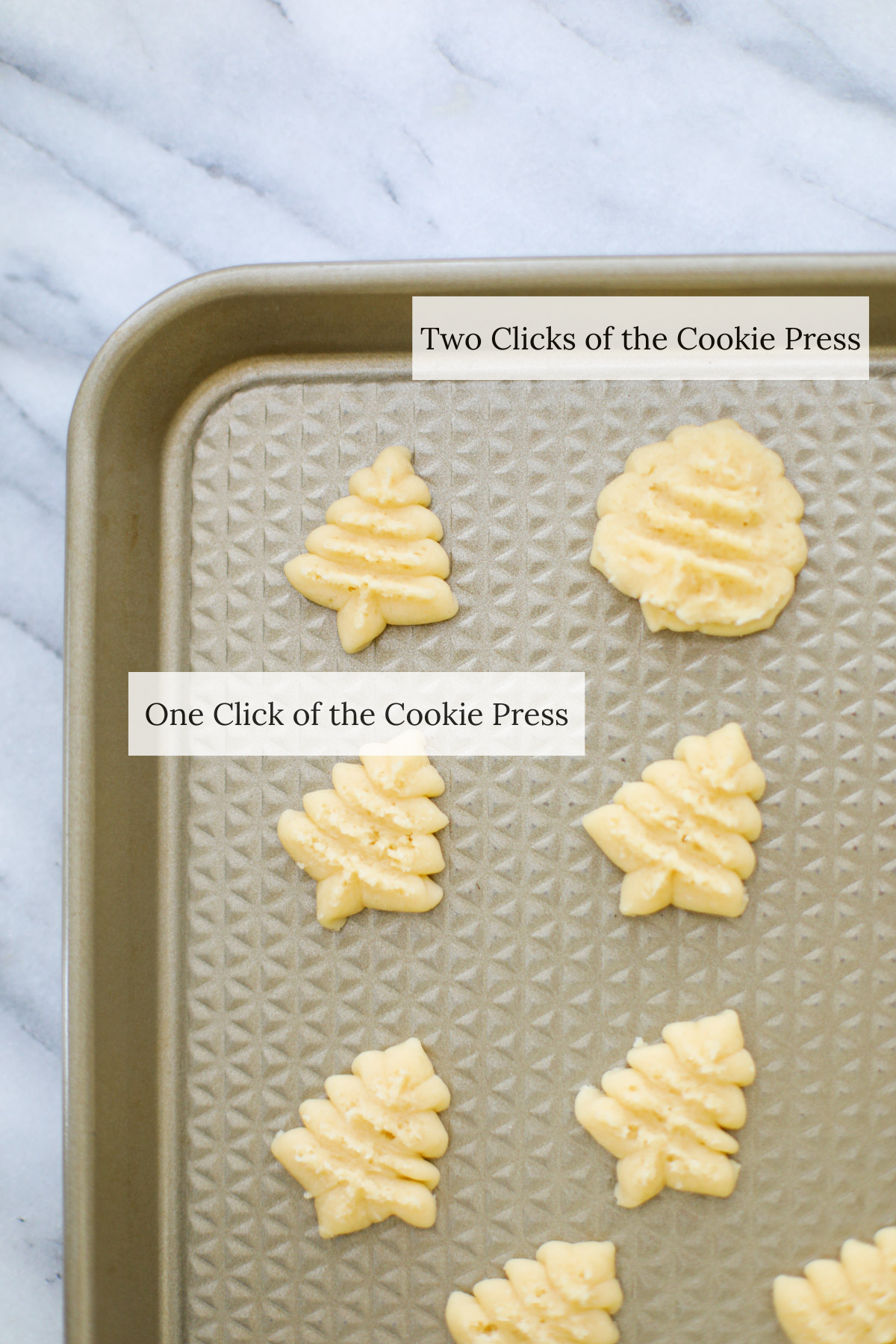 A gold baking sheet with spritz cookie dough christmas trees.