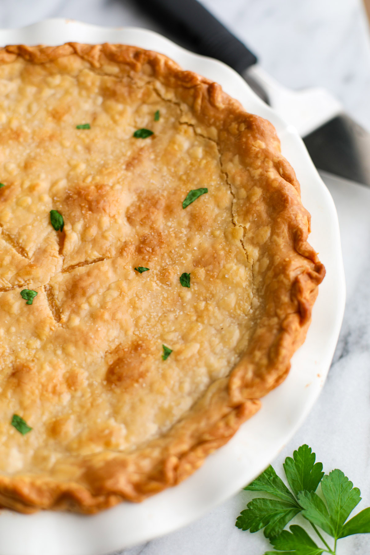 A close up of pot pie crust topped with little pieces of parsley and kosher salt. 