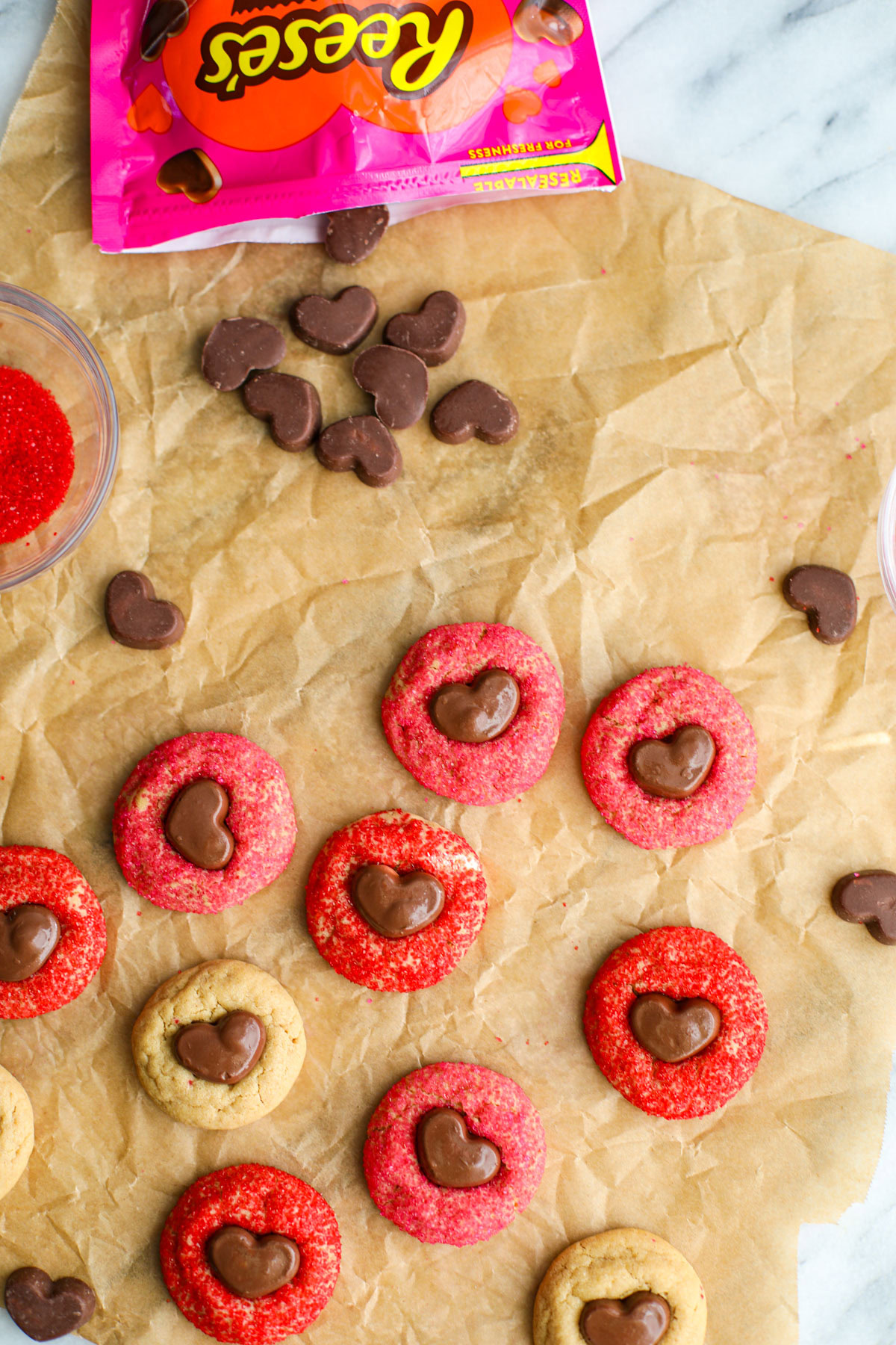 Red, pink, and plain peanut butter Cookies with mini Reese's hearts on crinkly brown parchment paper. 