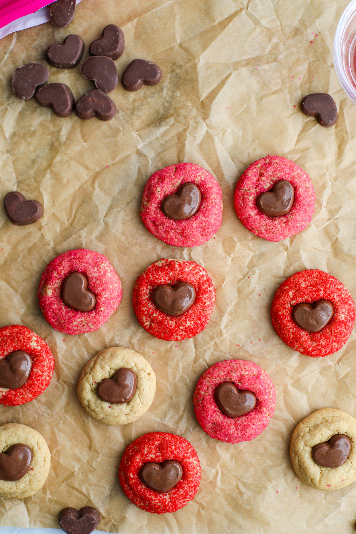 Red, pink, and plain peanut butter Cookies with mini Reese's hearts on crinkly brown parchment paper. 