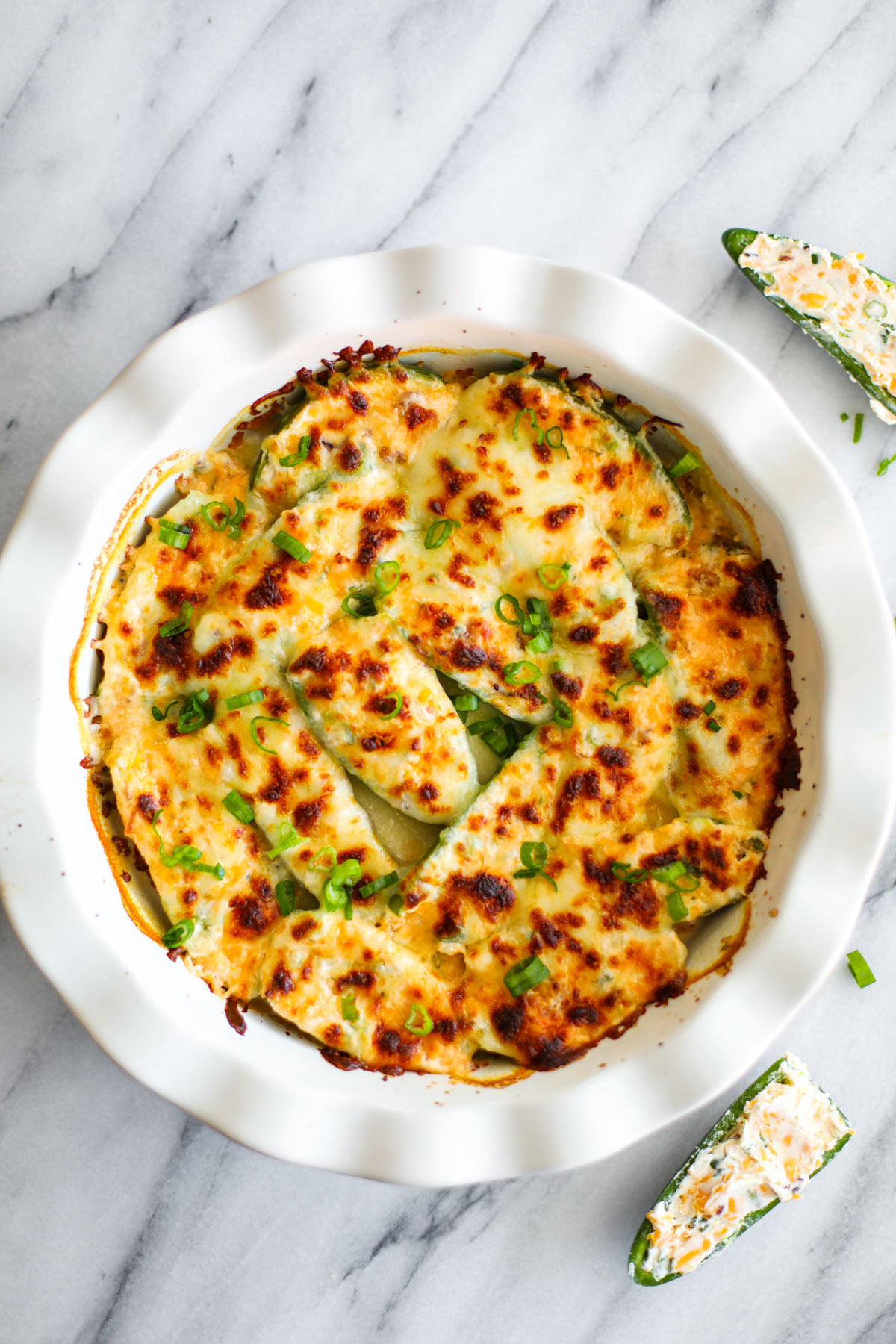 A white ruffled pie dish with golden jalapeño poppers topped with slices of green onions.