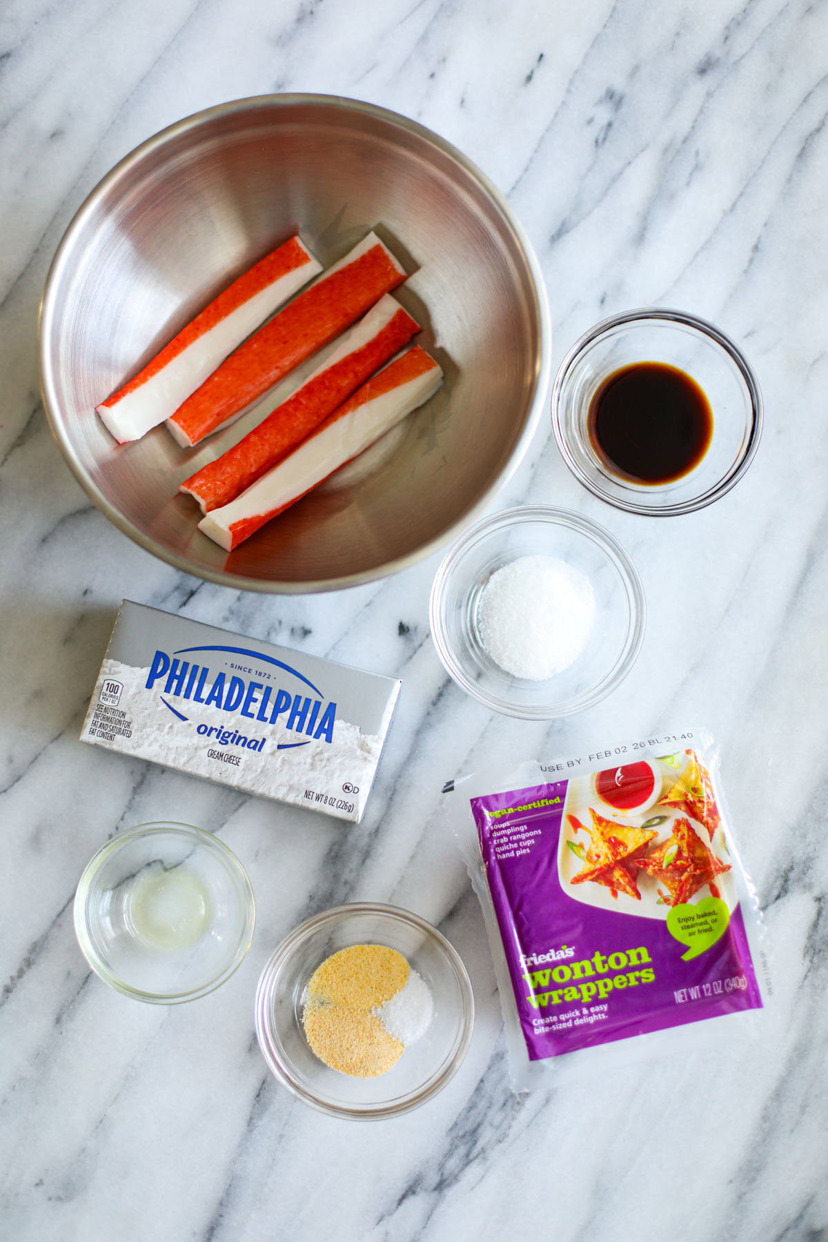 A stainless steel bowl filled with imitation crab legs, clear bowls of soy sauce, sugar, seasonings, sesame oil, and a package of Philadelphia cream cheese. 