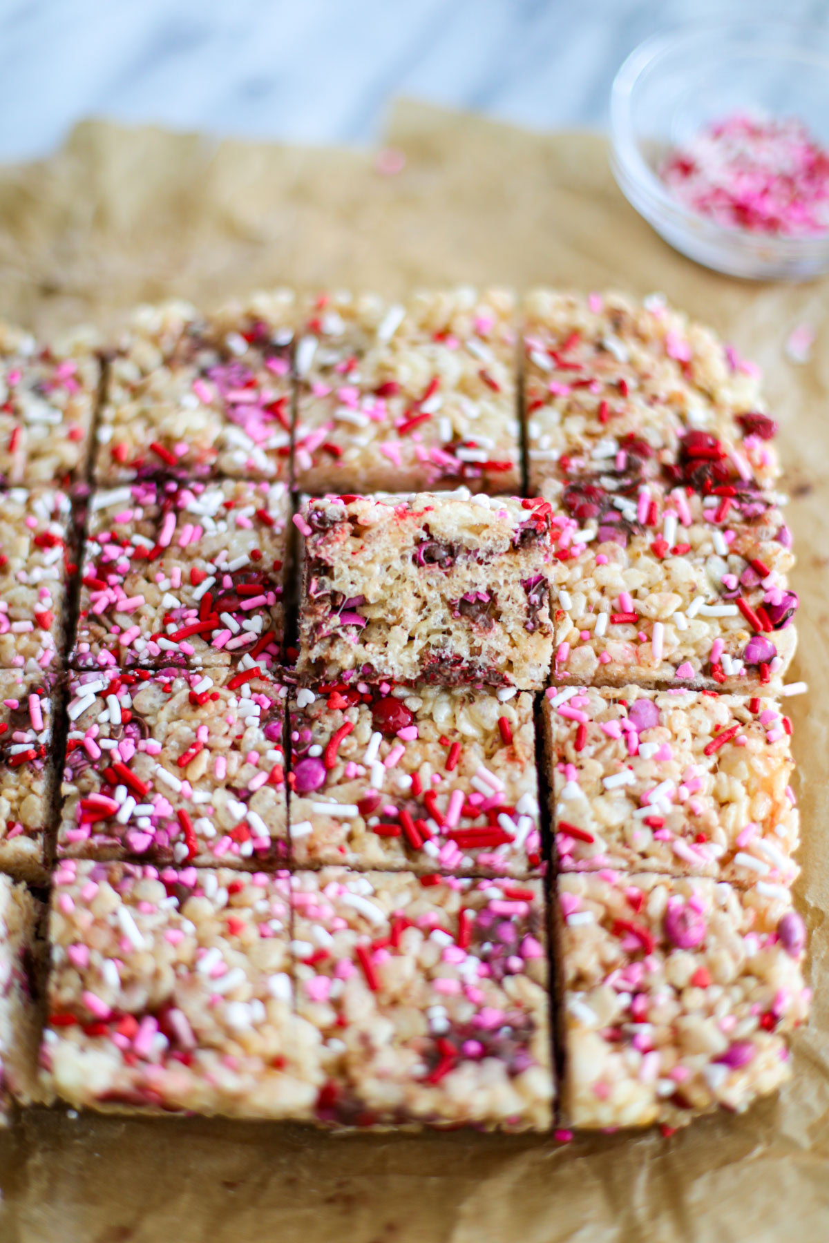 Pink, red, and white sprinkled Valentine's Mini M&M Rice Krispie treats cut into small squares lined up.