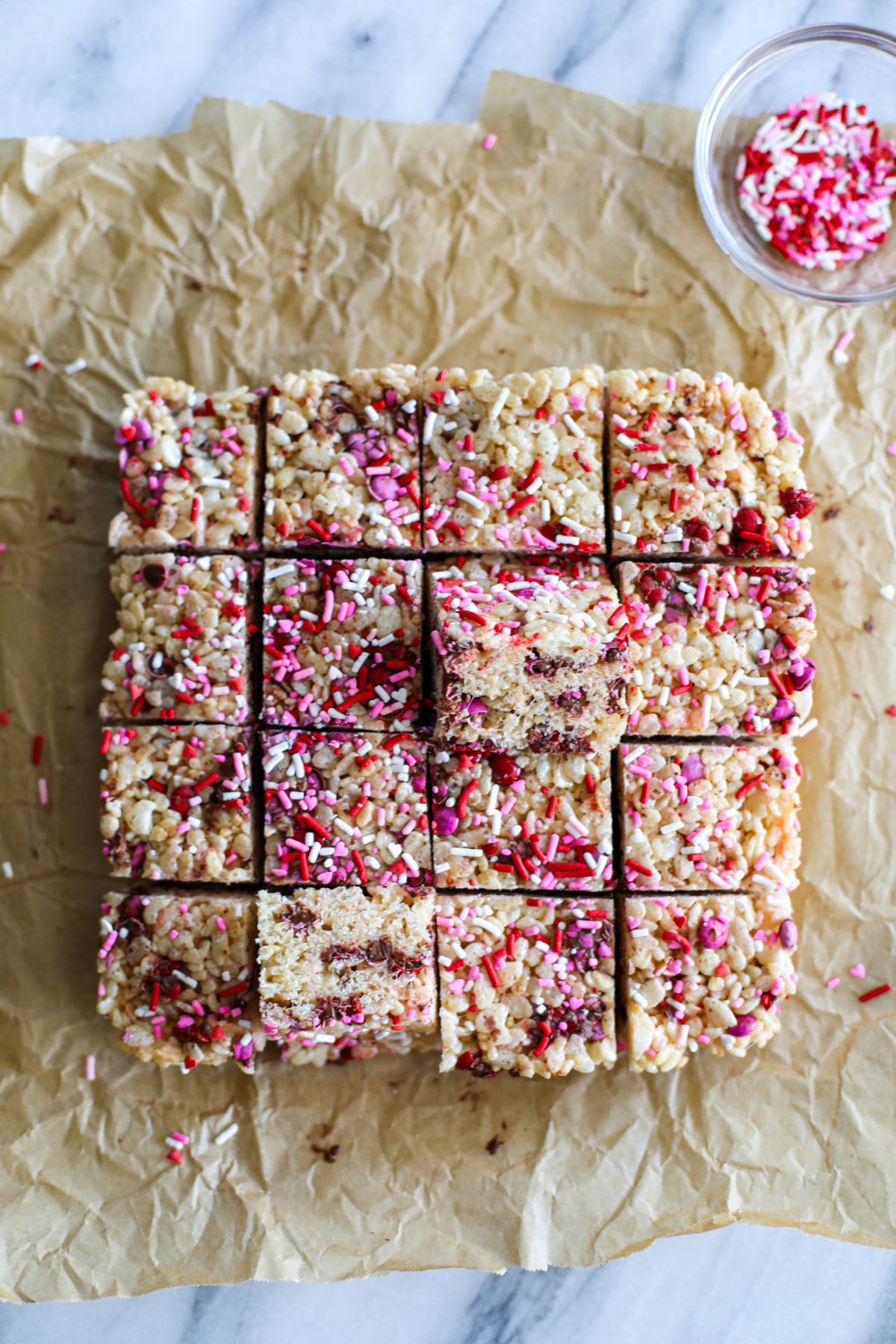 Pink, red, and white sprinkled Rice Krispie treats on brown parchment paper.