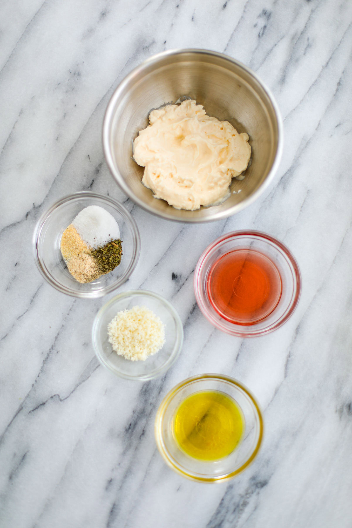 A stainless steel bowl of mayonnaise, and clear bowls of olive oil, red wine vinegar, spices, and parmigiano. 
