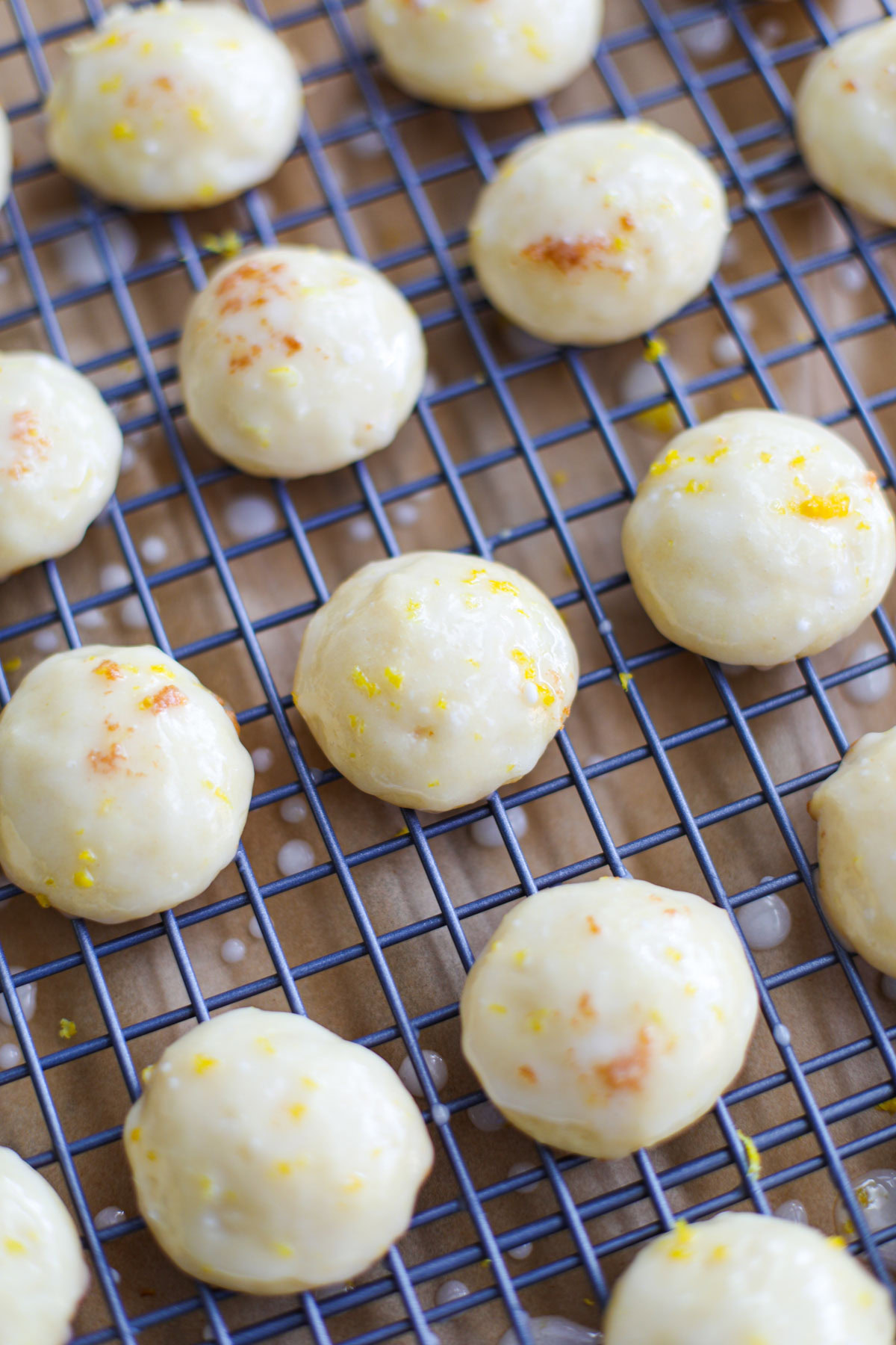 Glazed lemon ricotta cookies topped with lemon zest on a blue wire rack.