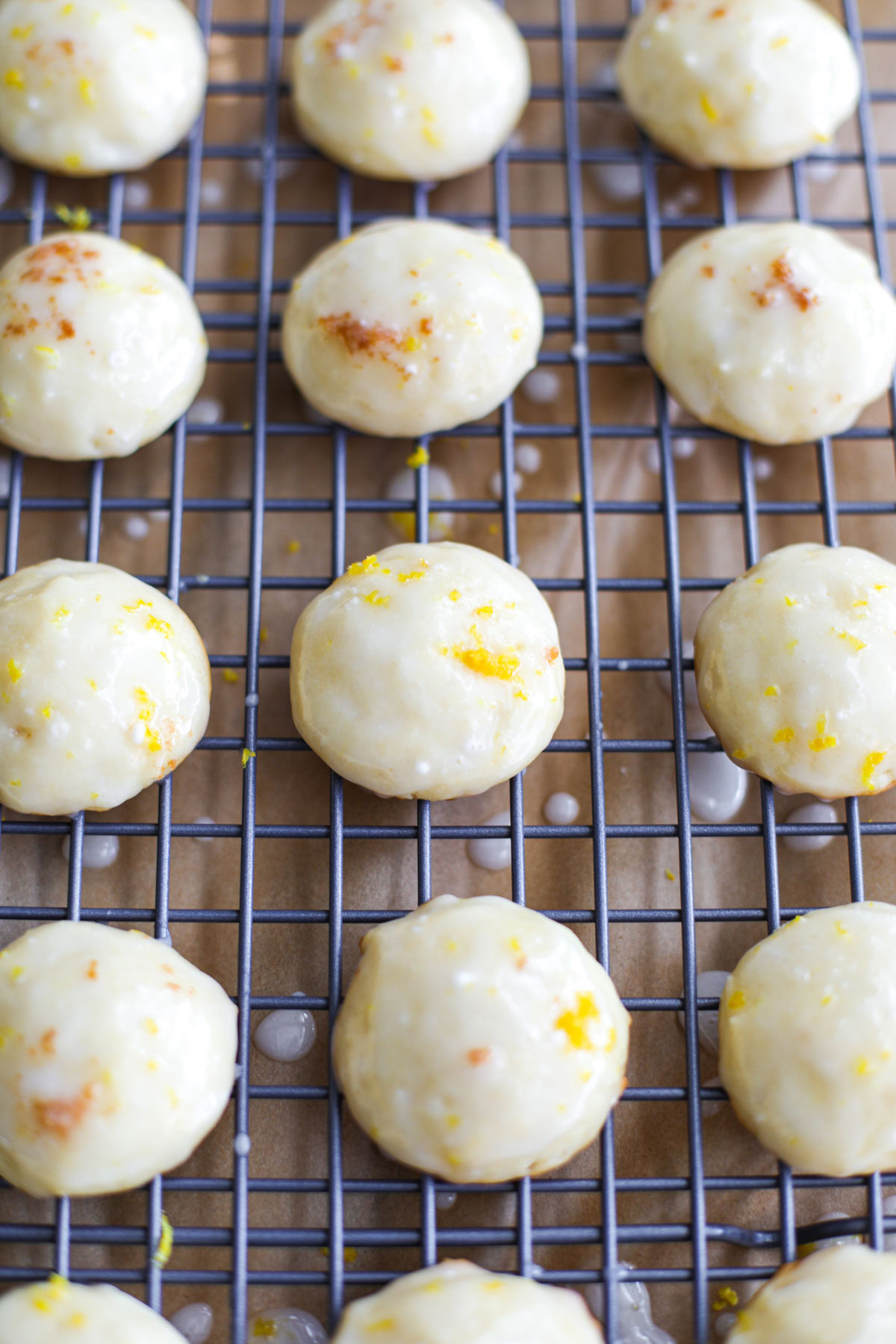 Glazed lemon ricotta cookies topped with lemon zest on a blue wire rack.