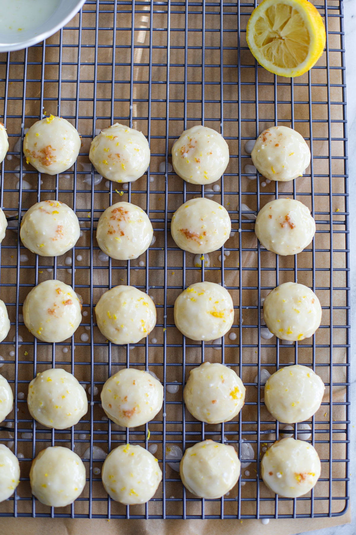 Glazed lemon ricotta cookies topped with lemon zest on a blue wire rack.