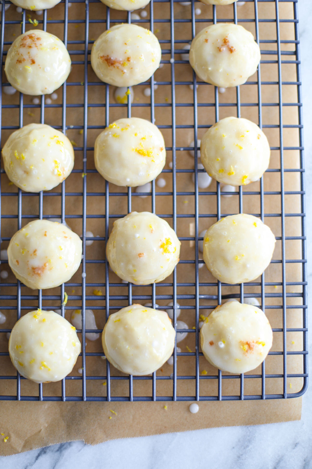 Glazed lemon ricotta cookies topped with lemon zest on a blue wire rack.