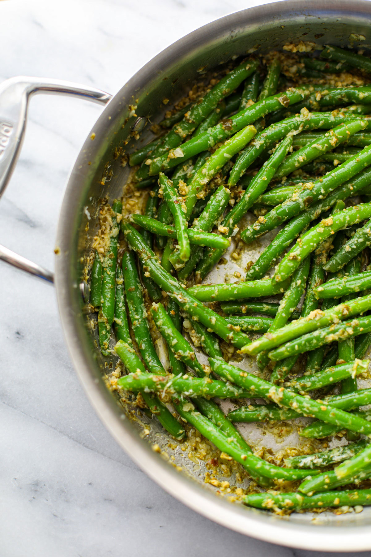 Pesto green beans in a large metal skillet on a white marble counter.