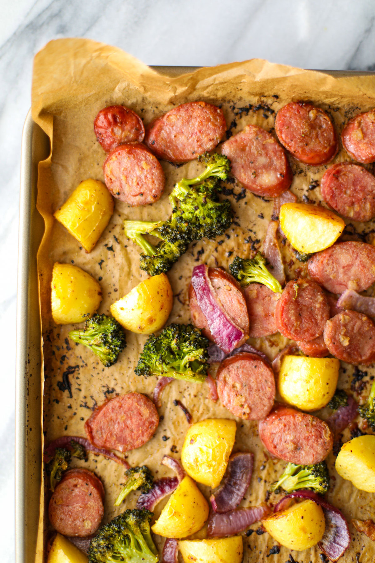 A chicken sausage sheet pan dinner with baby gold potatoes, broccoli florets, and sliced red onion.