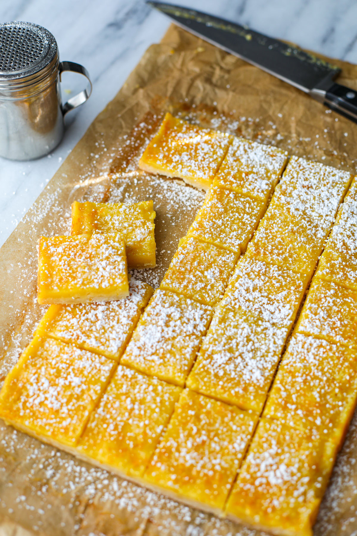 A tray of orange bars all sliced up on parchment paper with a powdered sugar shaker and knife.