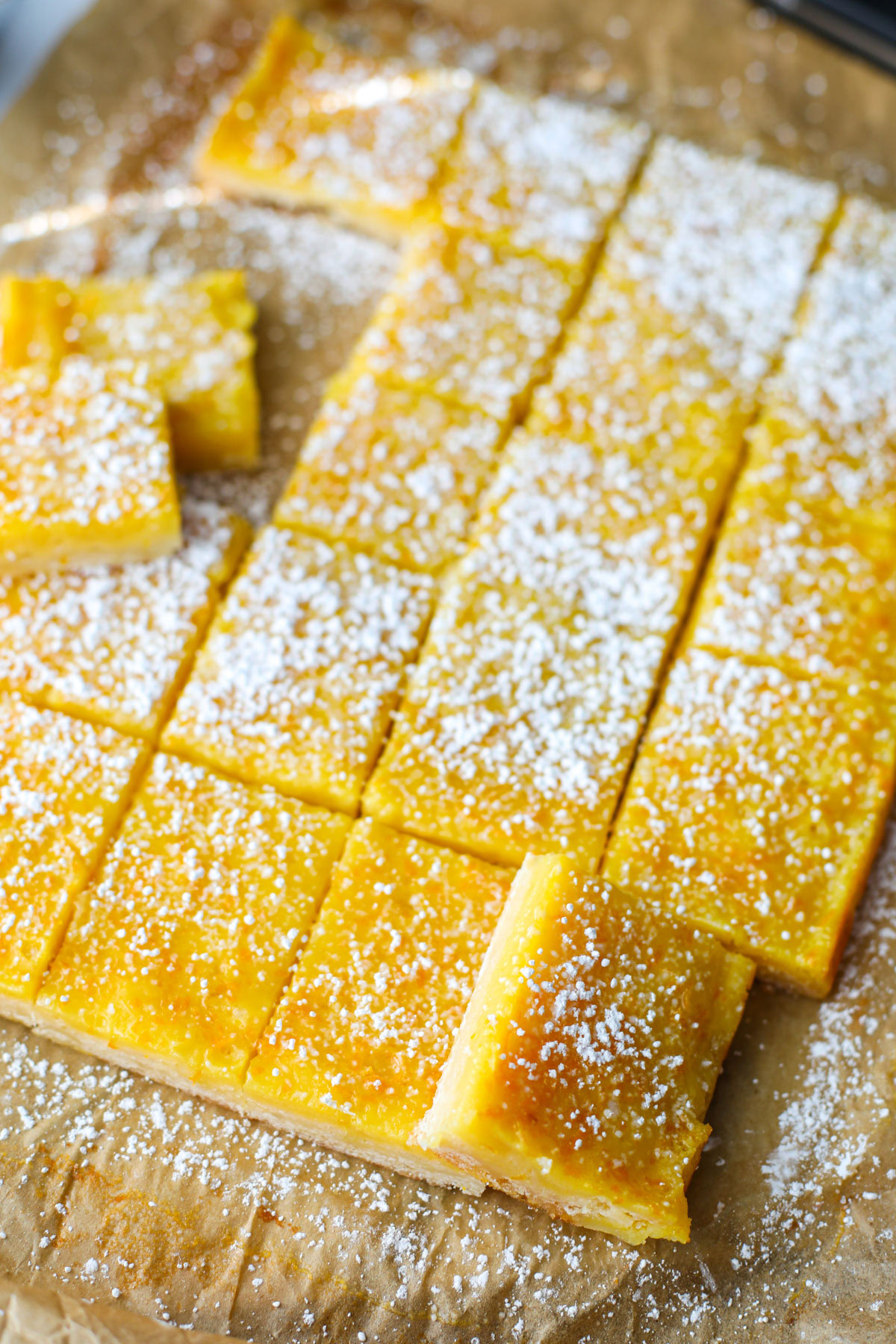 Rows of orange bars on parchment topped with powdered sugar. 