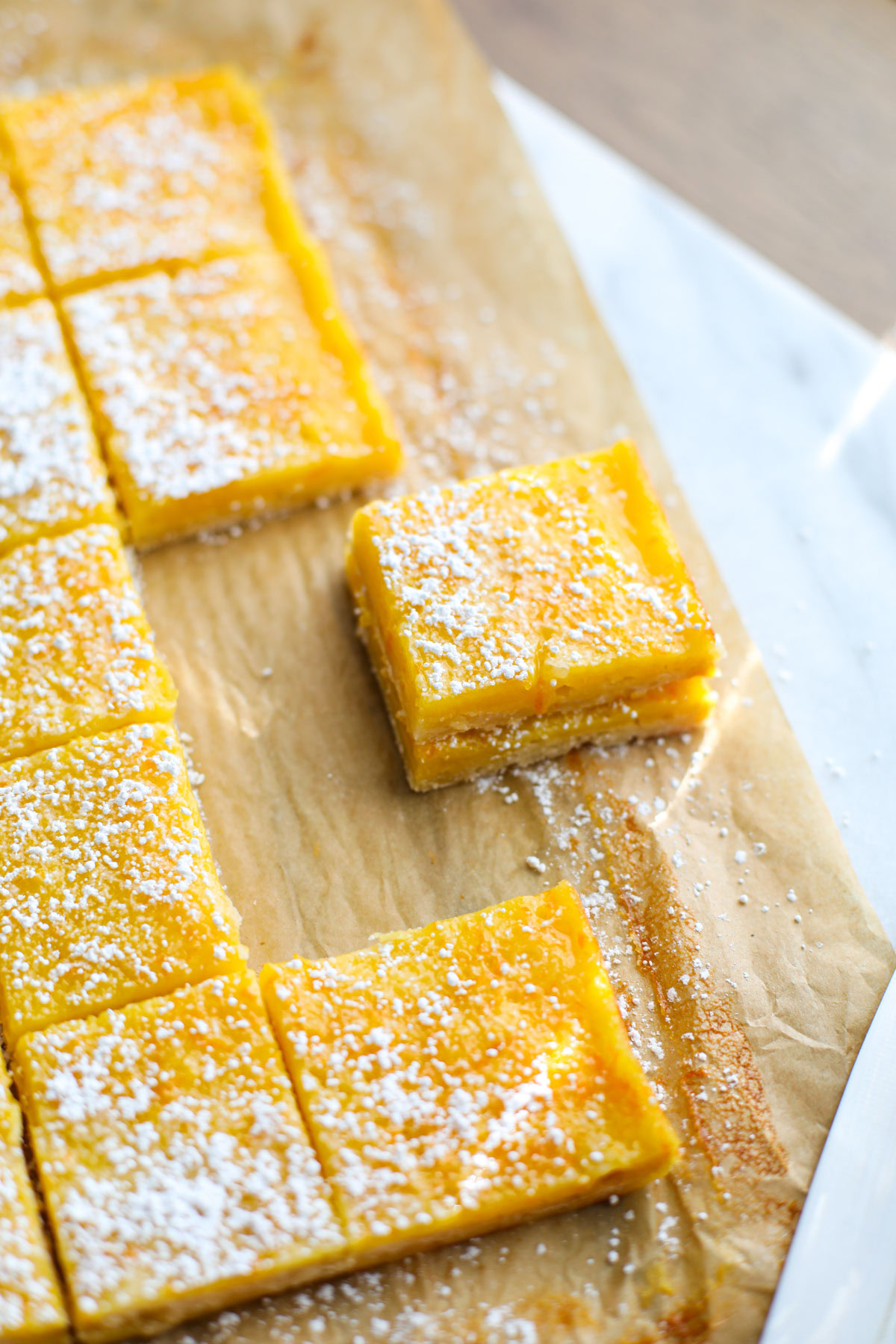 A stack of orange bars with powdered sugar on brown parchment paper.