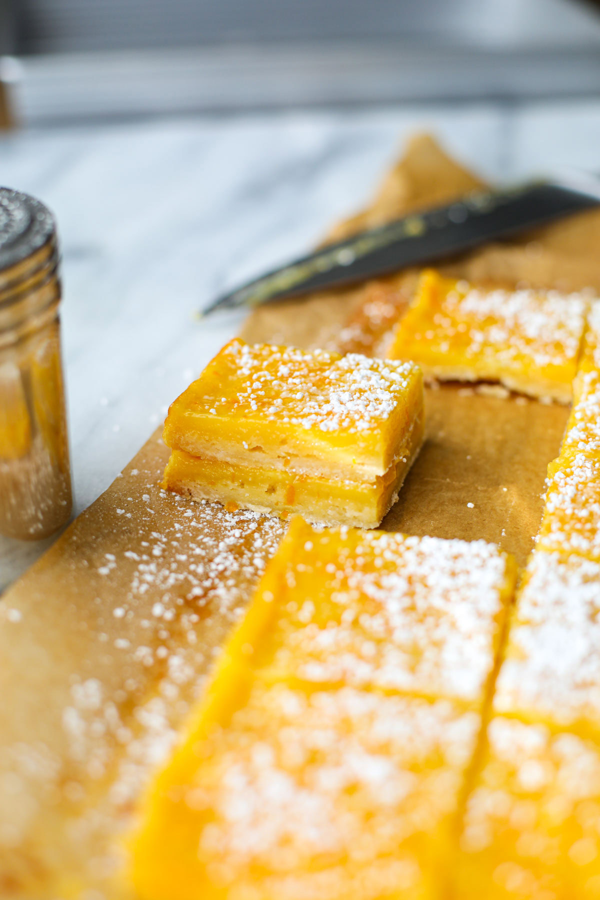A stack of orange bars with powdered sugar on brown parchment paper.