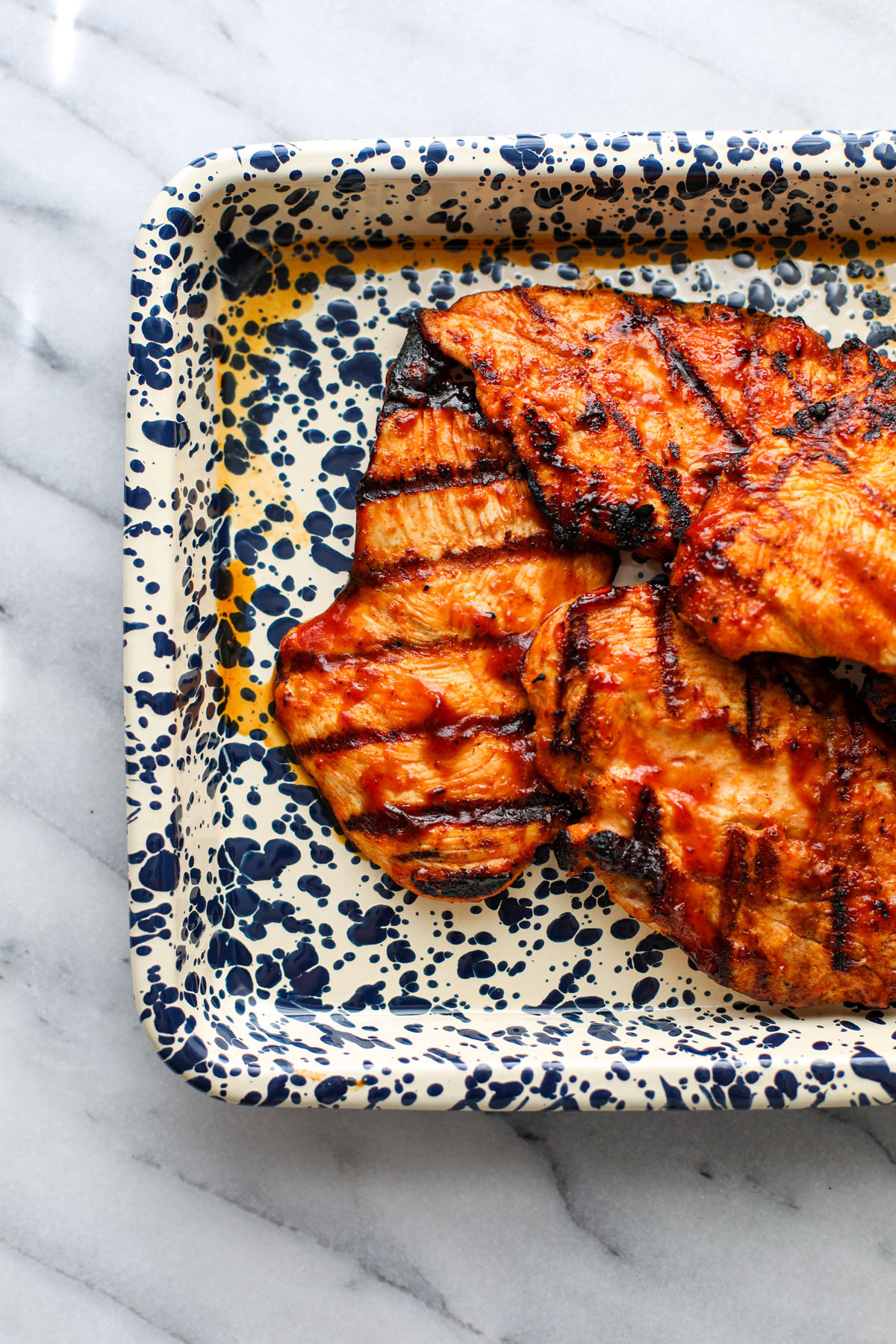 Grilled barbecue chicken on a white and blue splattered sheet tray.