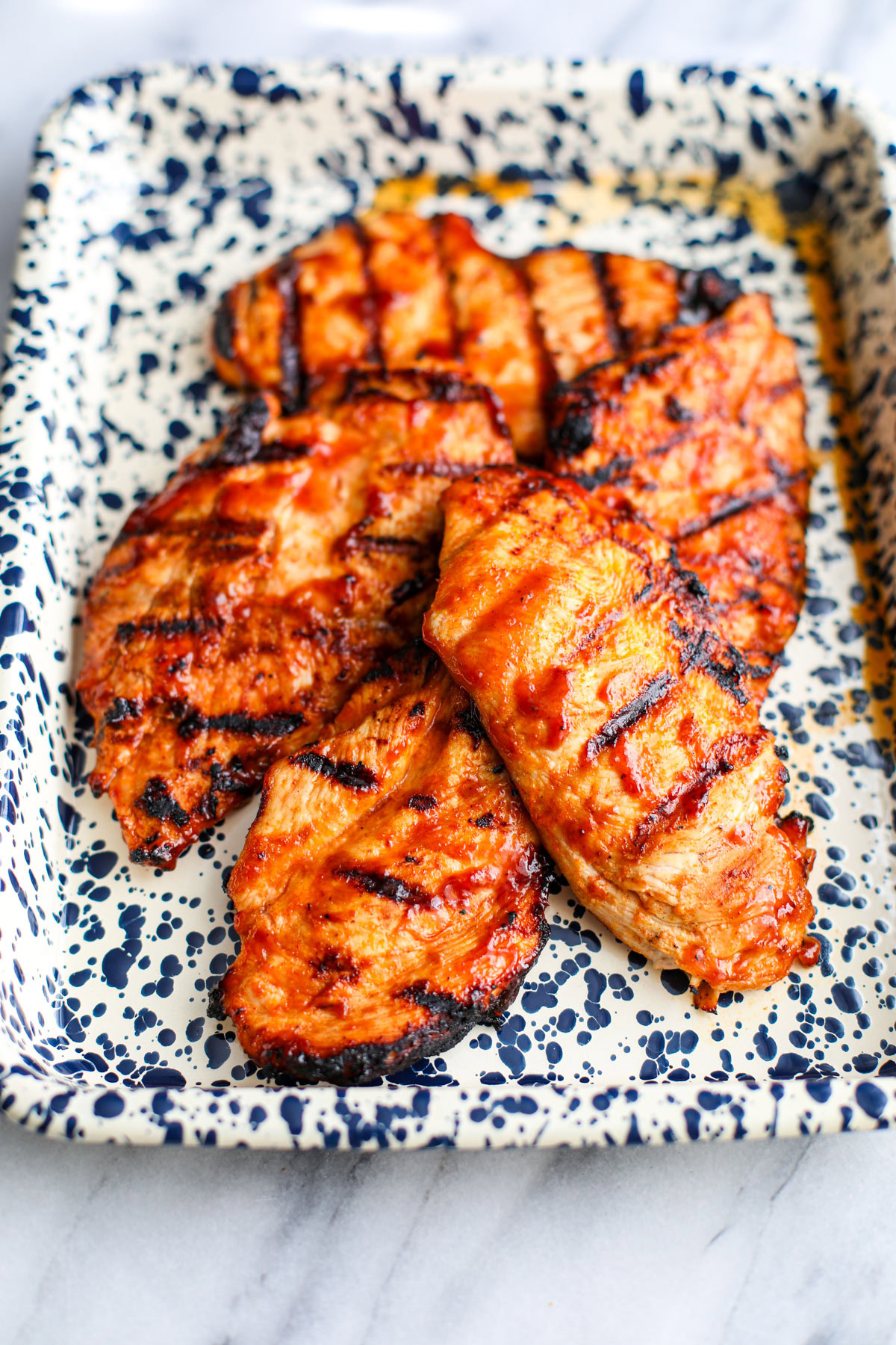 Grilled barbecue chicken on a white and blue splattered sheet tray.