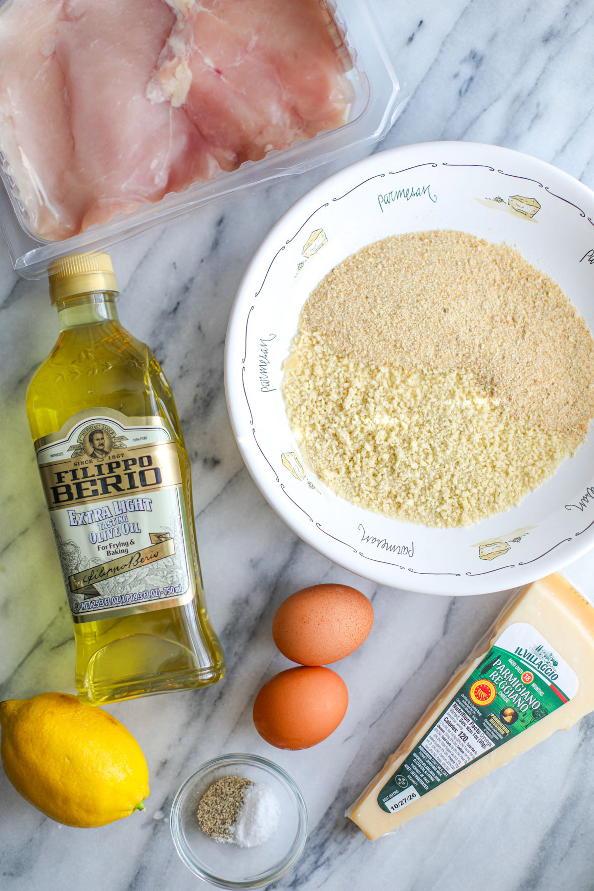 Ingredients to make chicken milanese including cutlets, breadcrumbs, oil, eggs, parmesan, lemon, and seasonings.