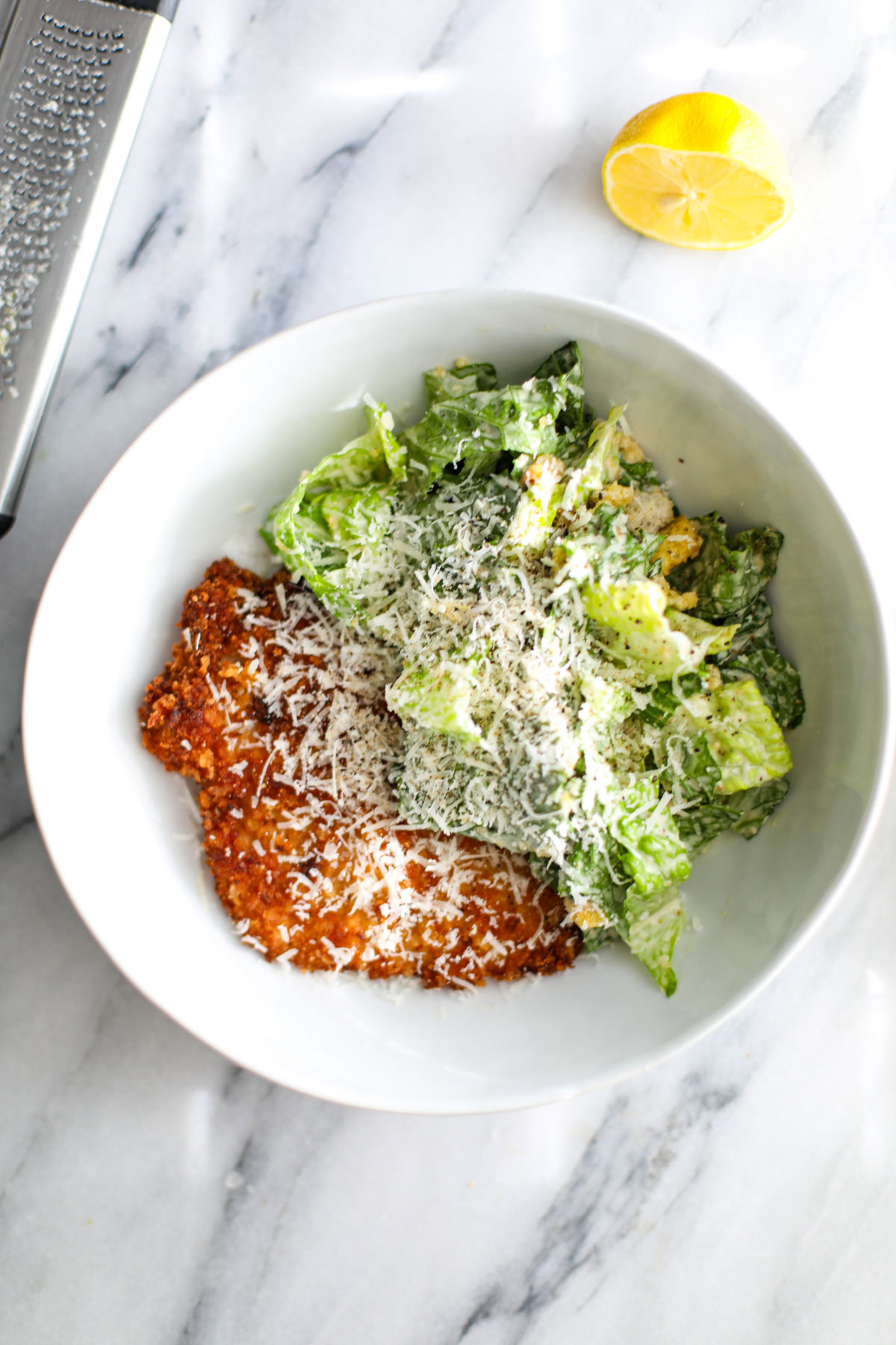Crispy chicken caesar salad in a white bowl next to half a lemon.