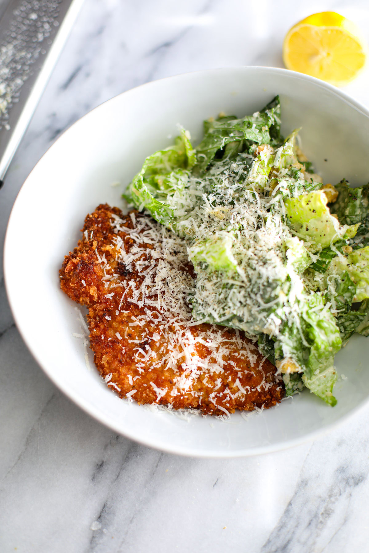 Crispy chicken caesar salad in a white bowl next to a microplane grater.