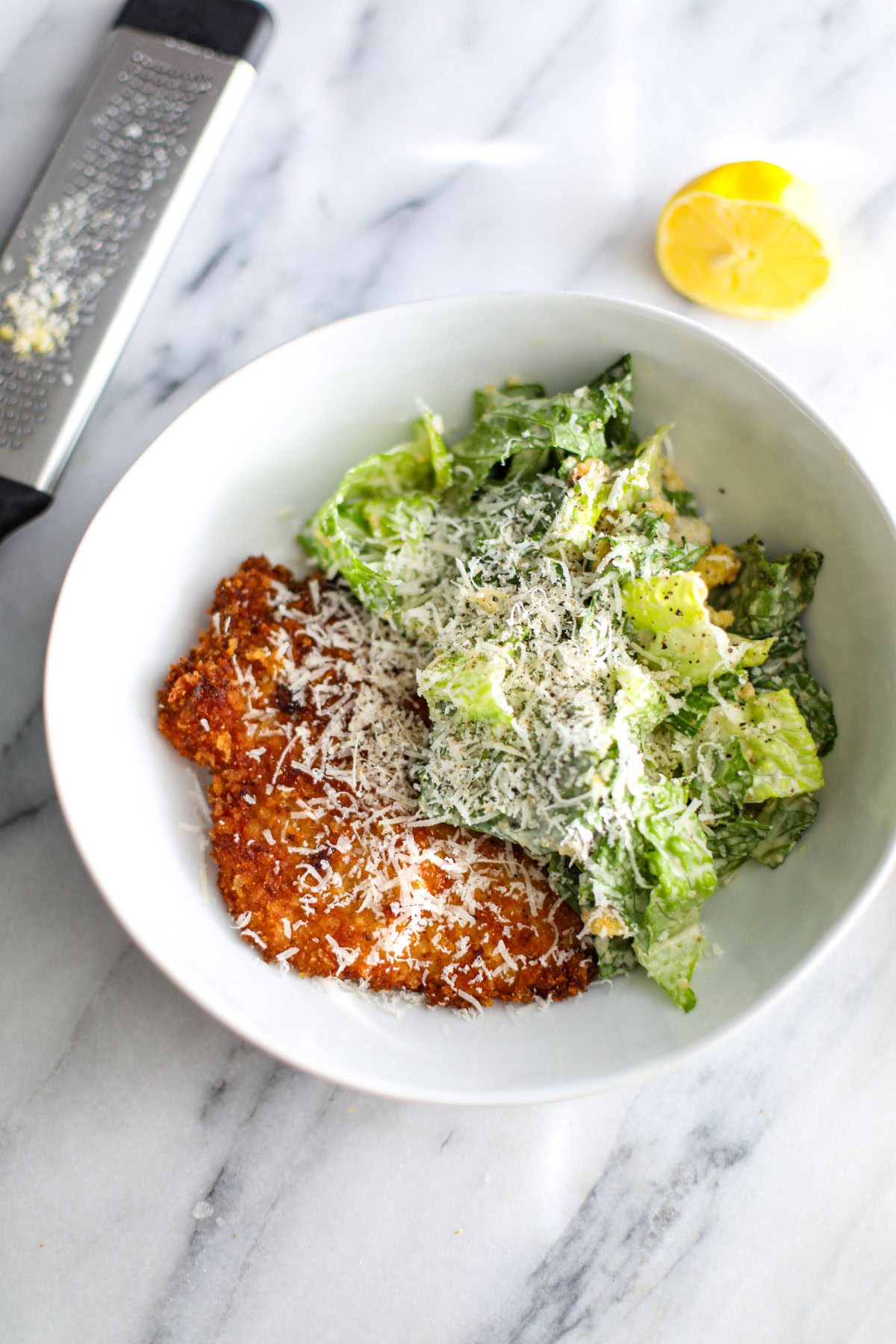 Crispy chicken caesar salad in a white bowl next to half a lemon.