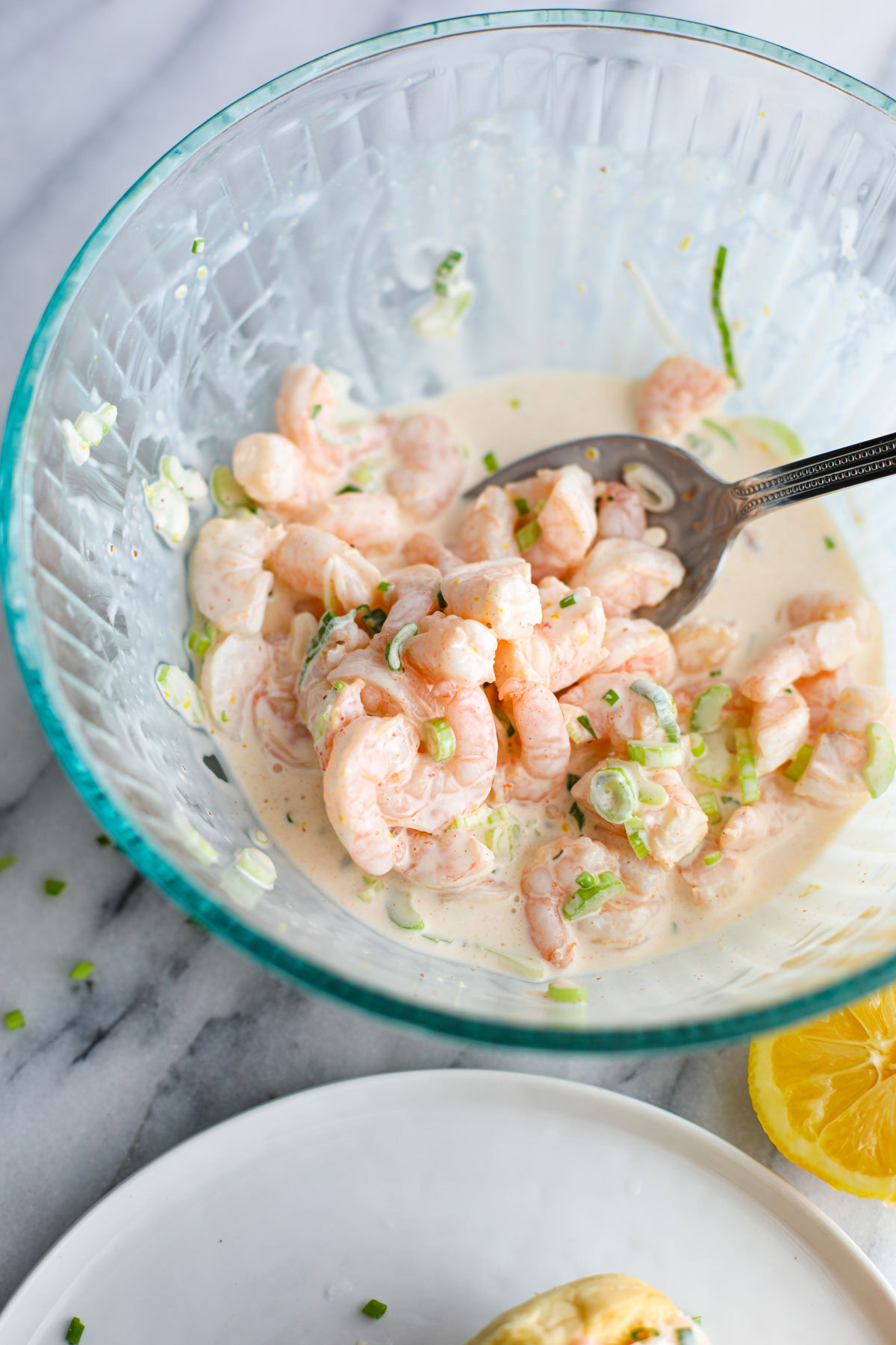 A blue glass bowl of shrimp tossed in a mayonnaise mixture used to top the rolls. 