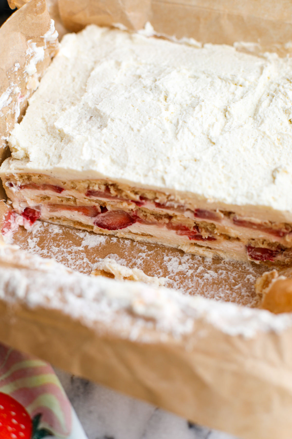 Strawberry shortcake icebox cake in a parchment lined baking dish showing the layers.