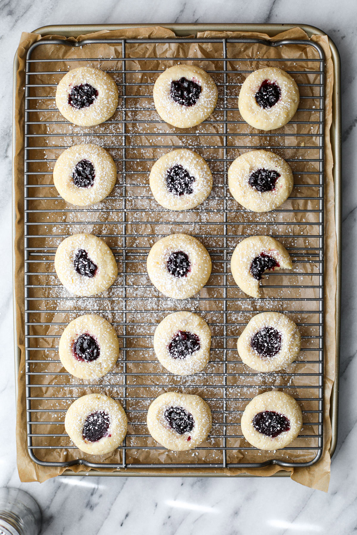 Blueberry thumbprint cookies on a cooling rack and cookie sheet.