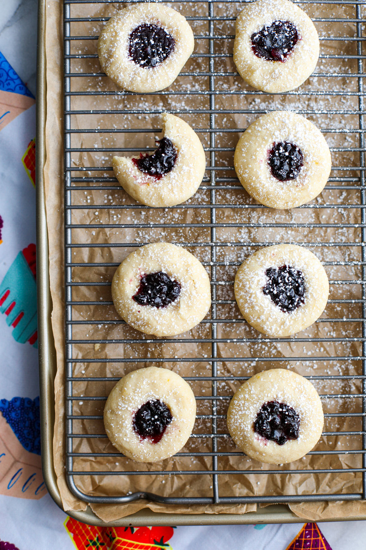 Blueberry thumbprint cookies on a cooling rack and cookie sheet.