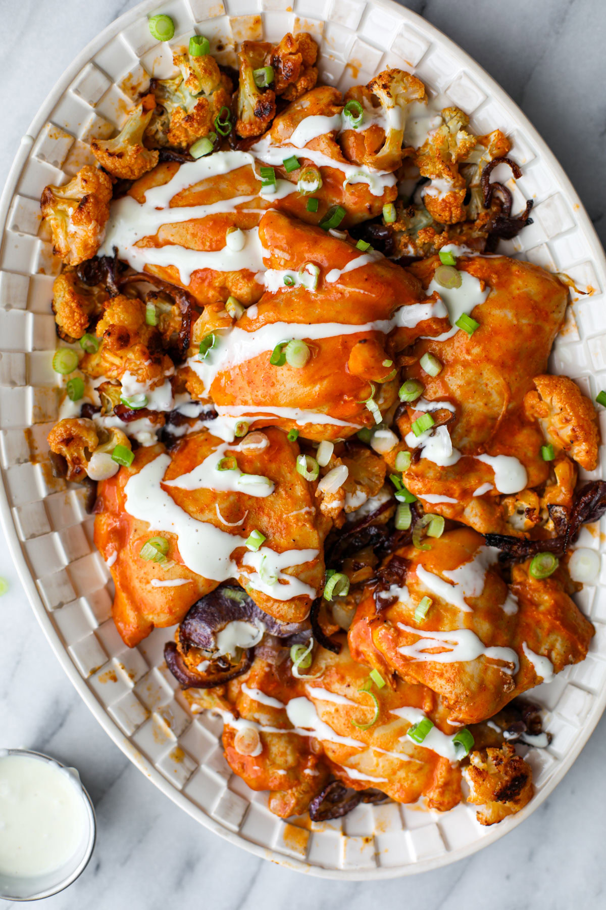 Buffalo Chicken thighs on a white platter drizzled with blue cheese and topped with green onions.