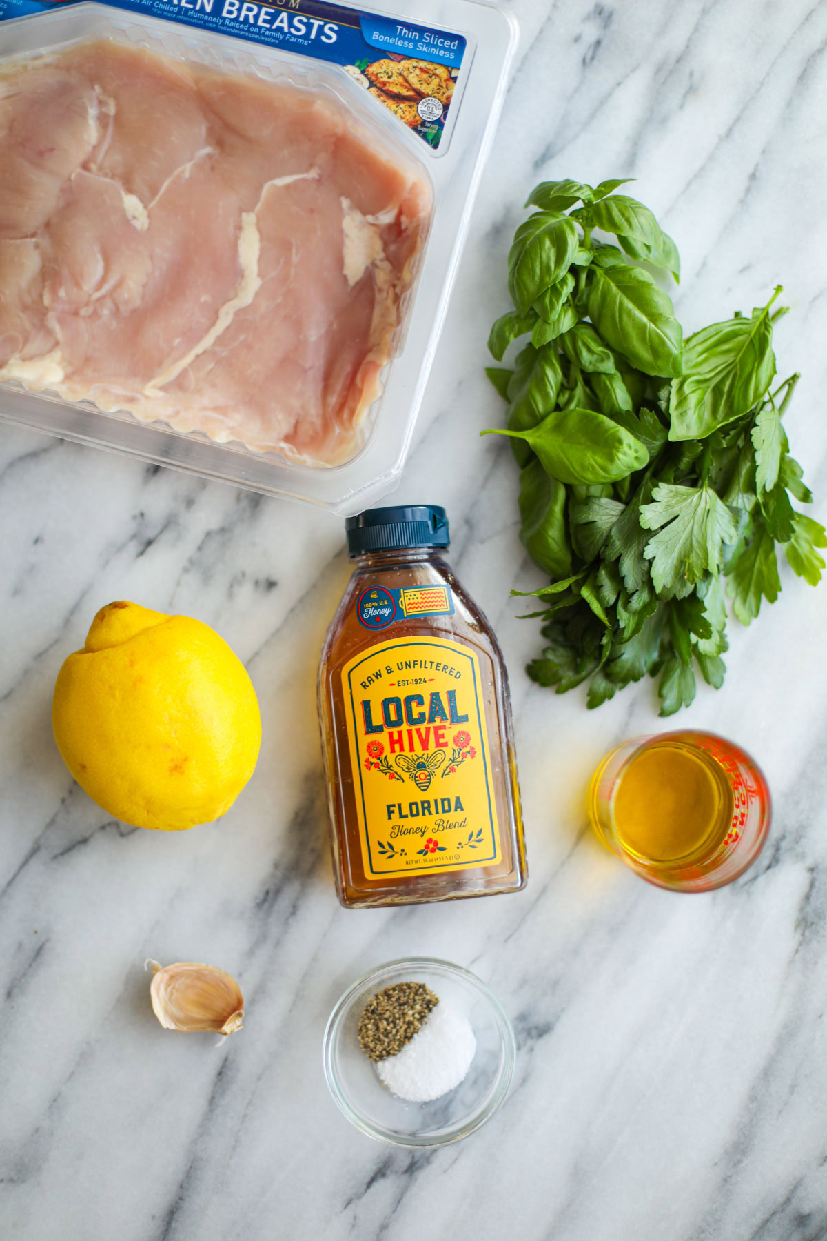 A package of chicken, fresh herbs, a lemon, honey, oil, and seasonings.