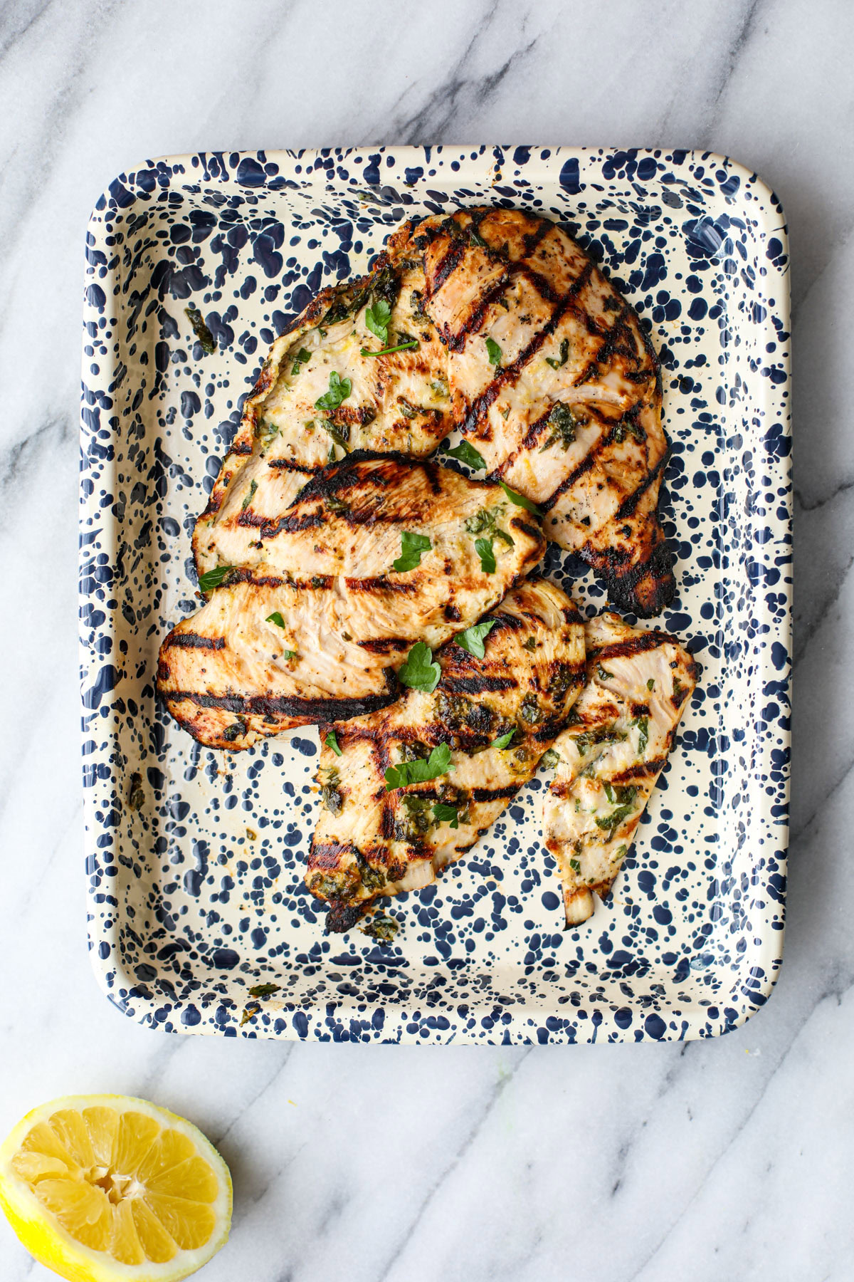 Herby grilled chicken marinade on a spotted platter with half a lemon.
