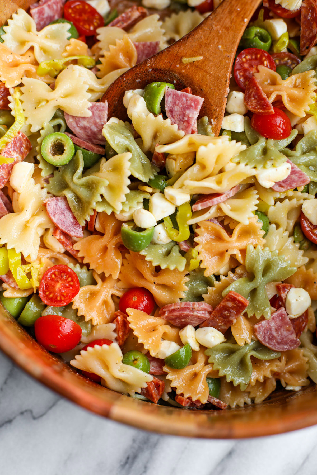 A wooden salad bowl of classic pasta salad with salad servers. 