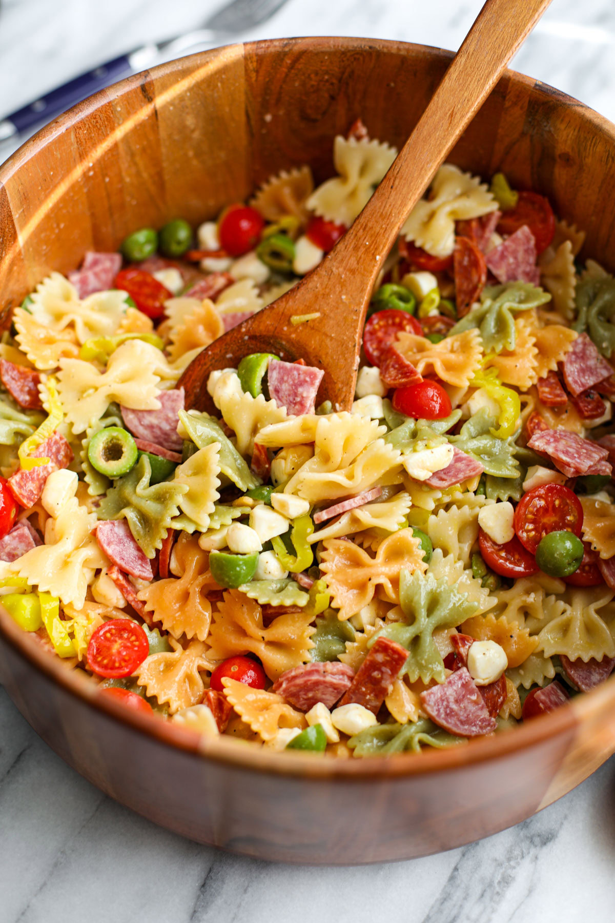 A wooden salad bowl of classic pasta salad with salad servers. 