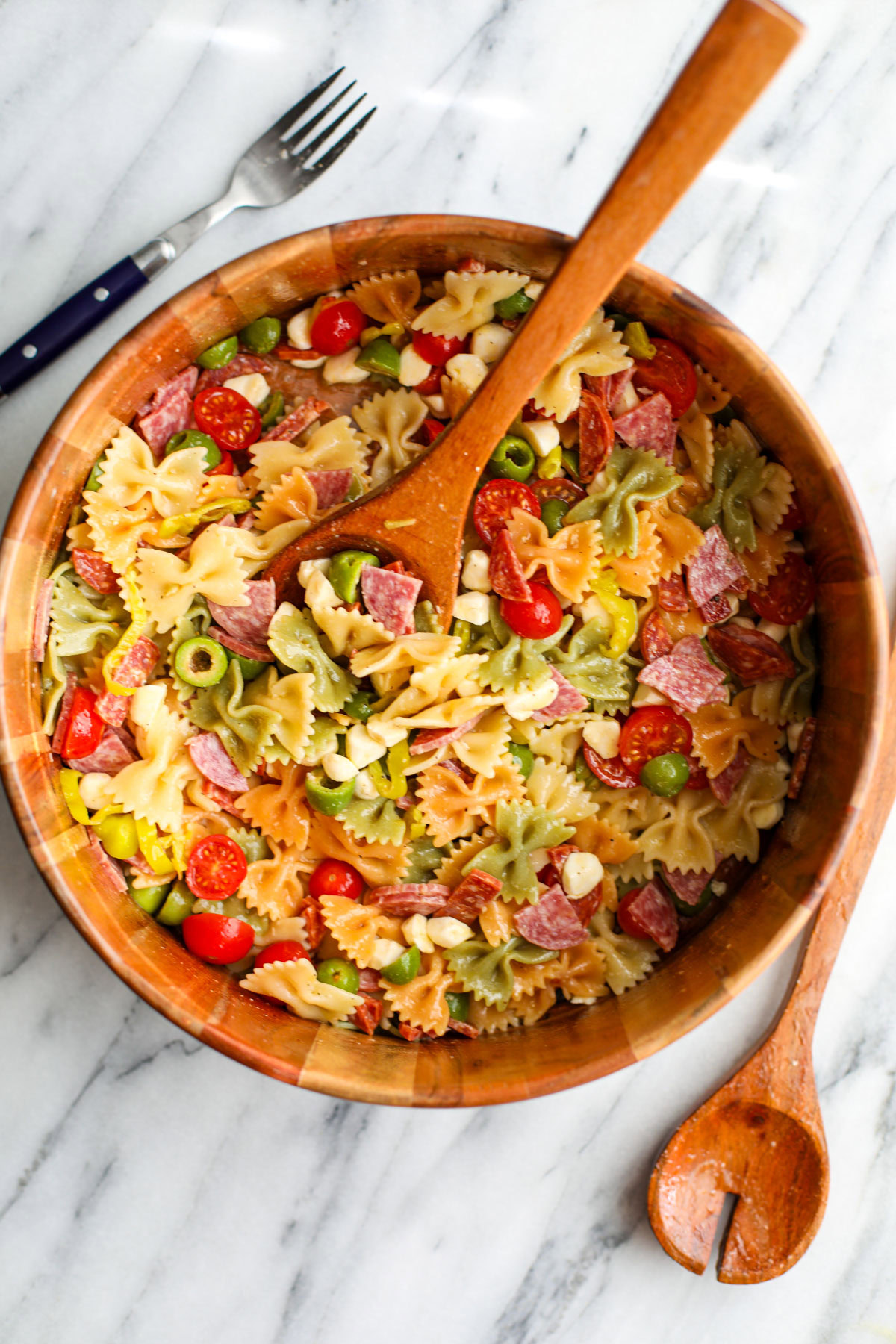 A wooden salad bowl of classic pasta salad with salad servers. 