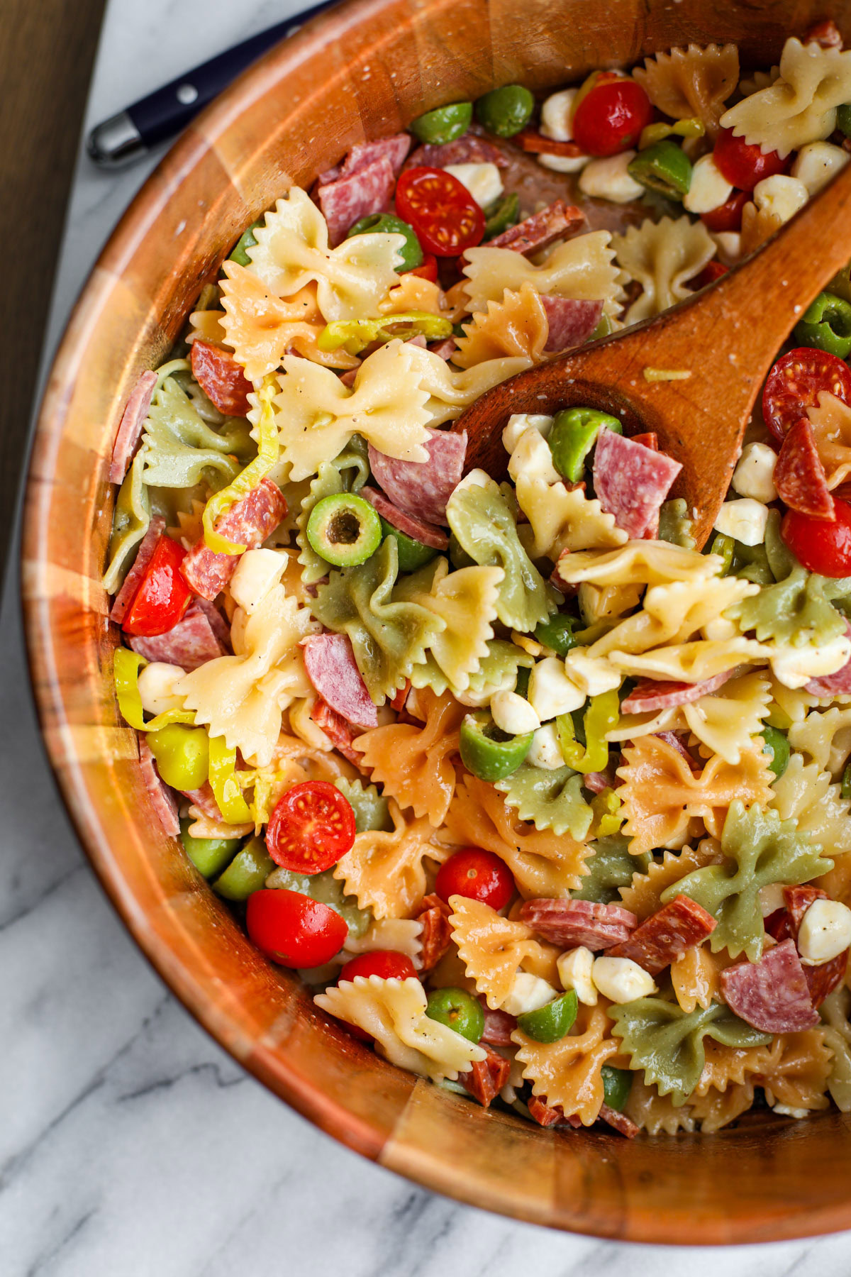 A wooden salad bowl of classic pasta salad with salad servers. 