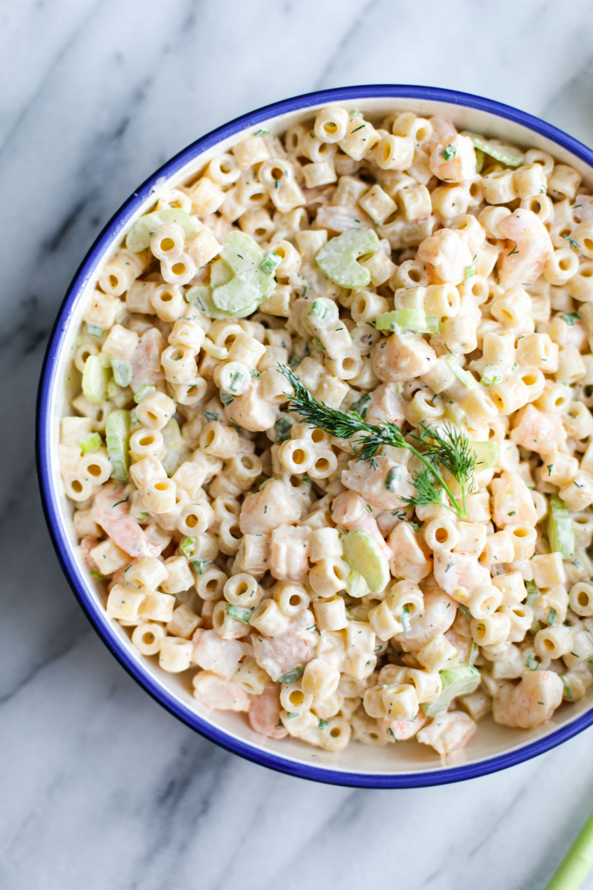 A blue bowl of shrimp pasta salad on a marble counter.