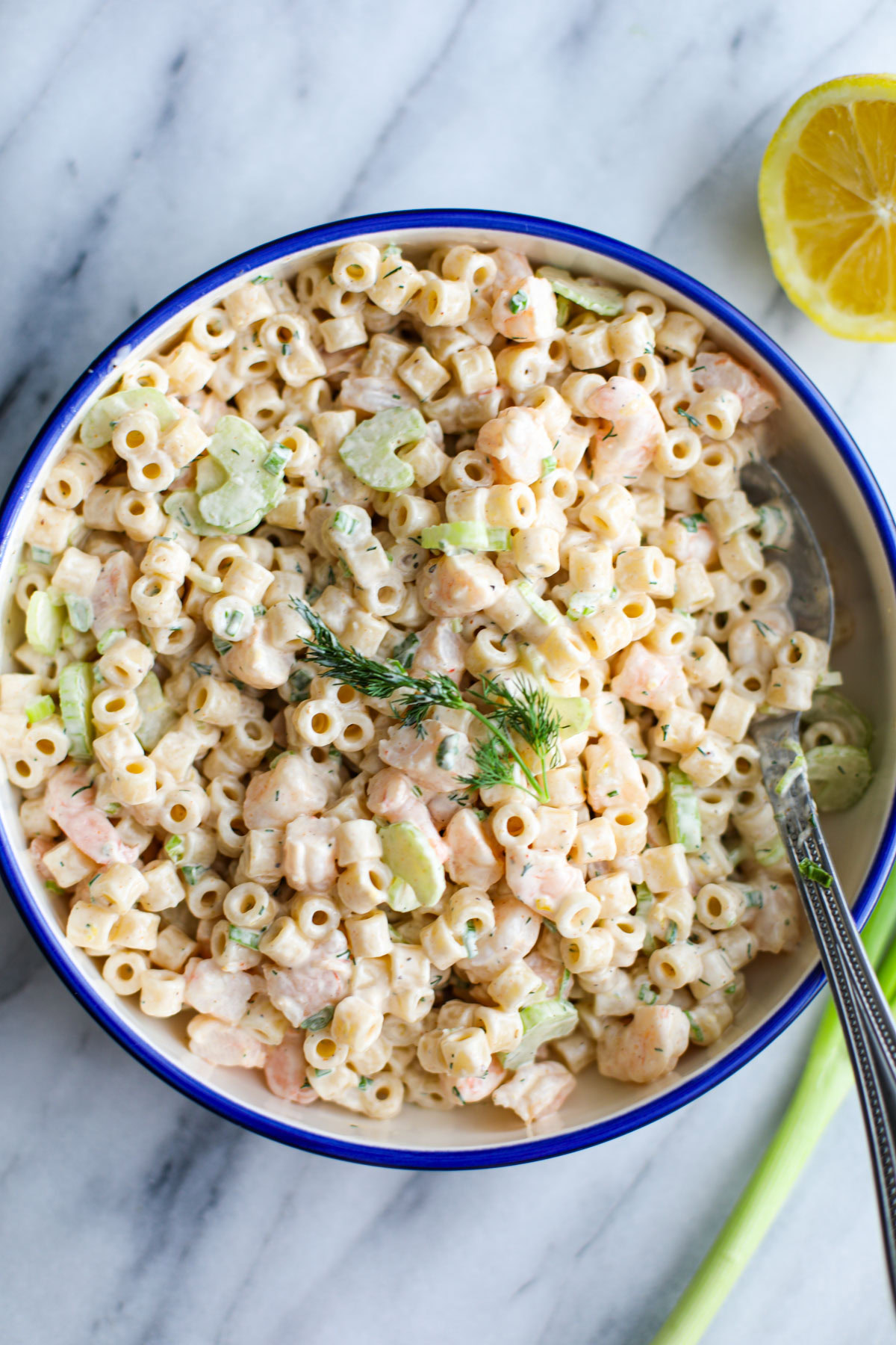 A blue bowl of shrimp pasta salad with a silver spoon.