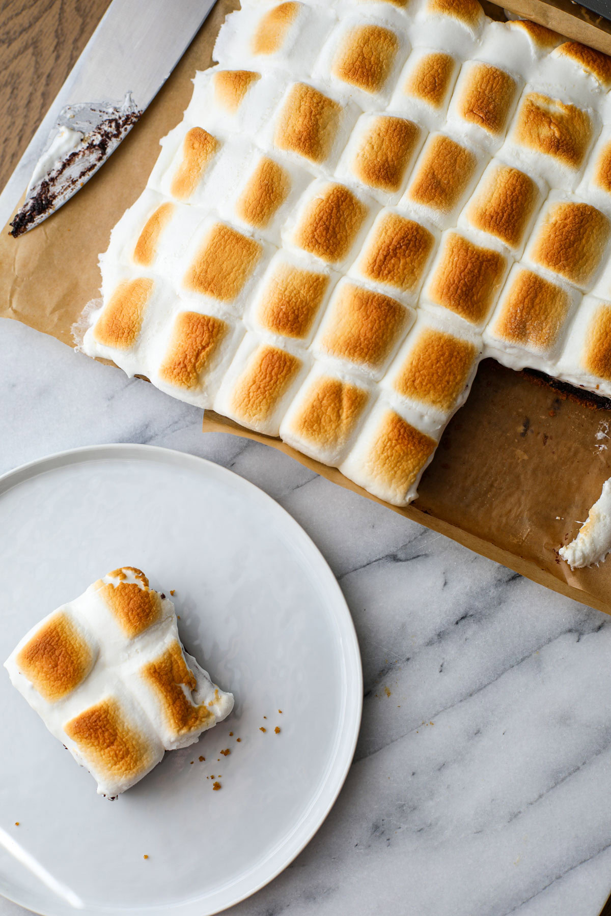 Smores brownies on parchment paper with a brownie on a white plate.